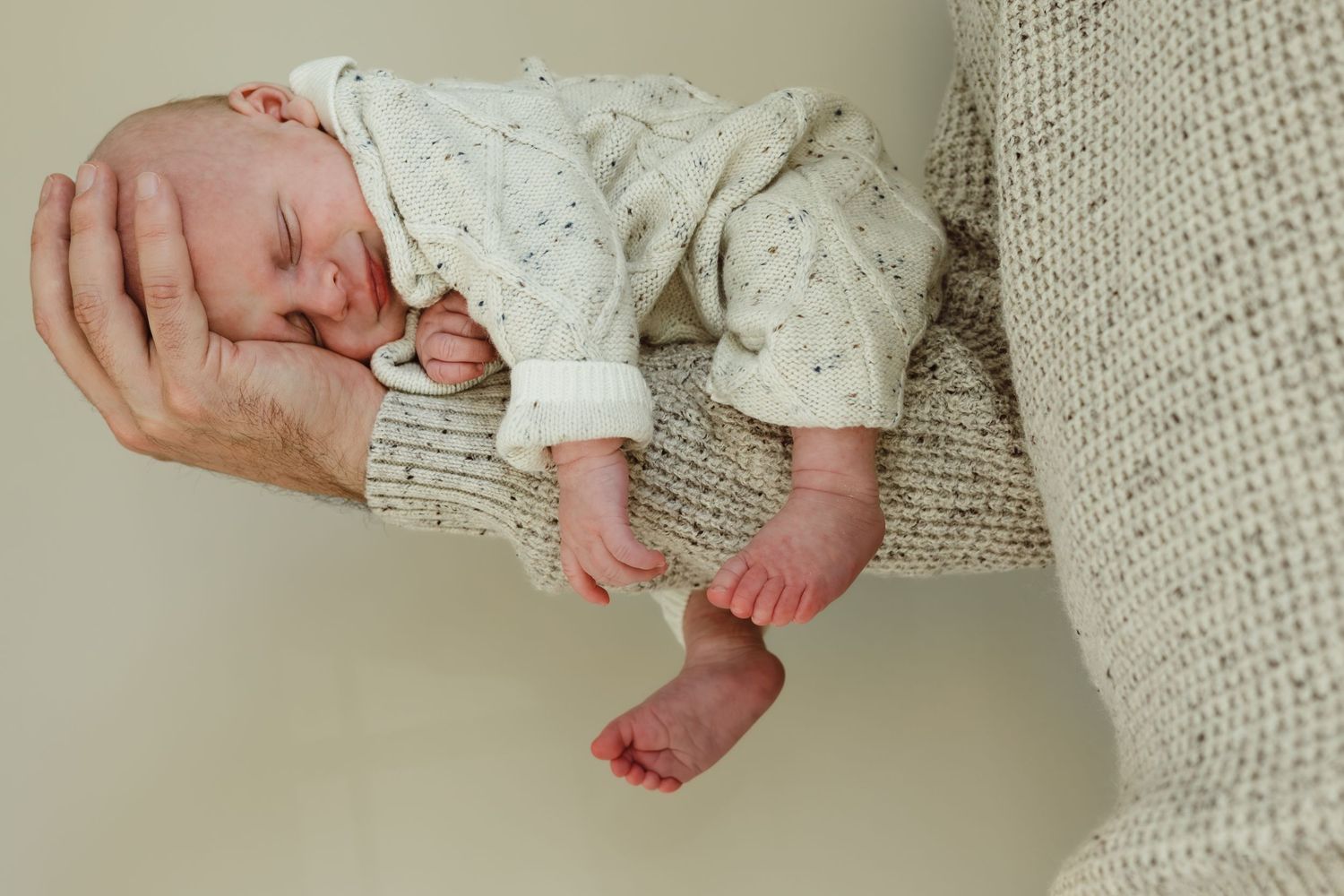 A newborn baby lays in fathers hand and arm with arms and feet dangling for a newborn photoshoot in Connecticut.