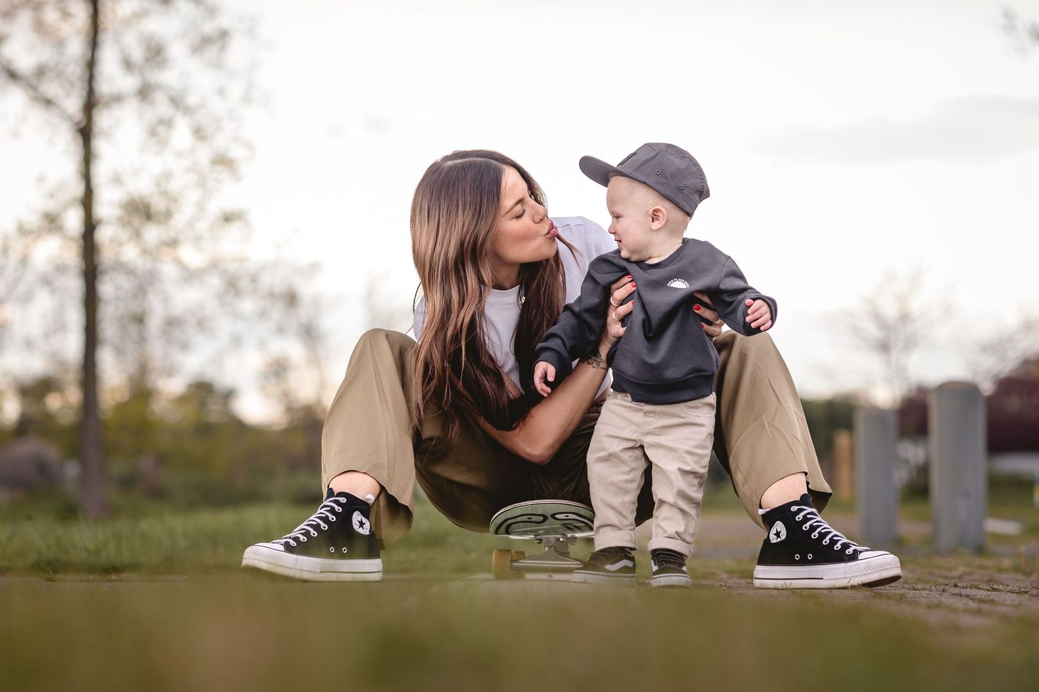 A mother and young son share tender moments together outdoors siting on skateboard during a milestone cake smash photo session.