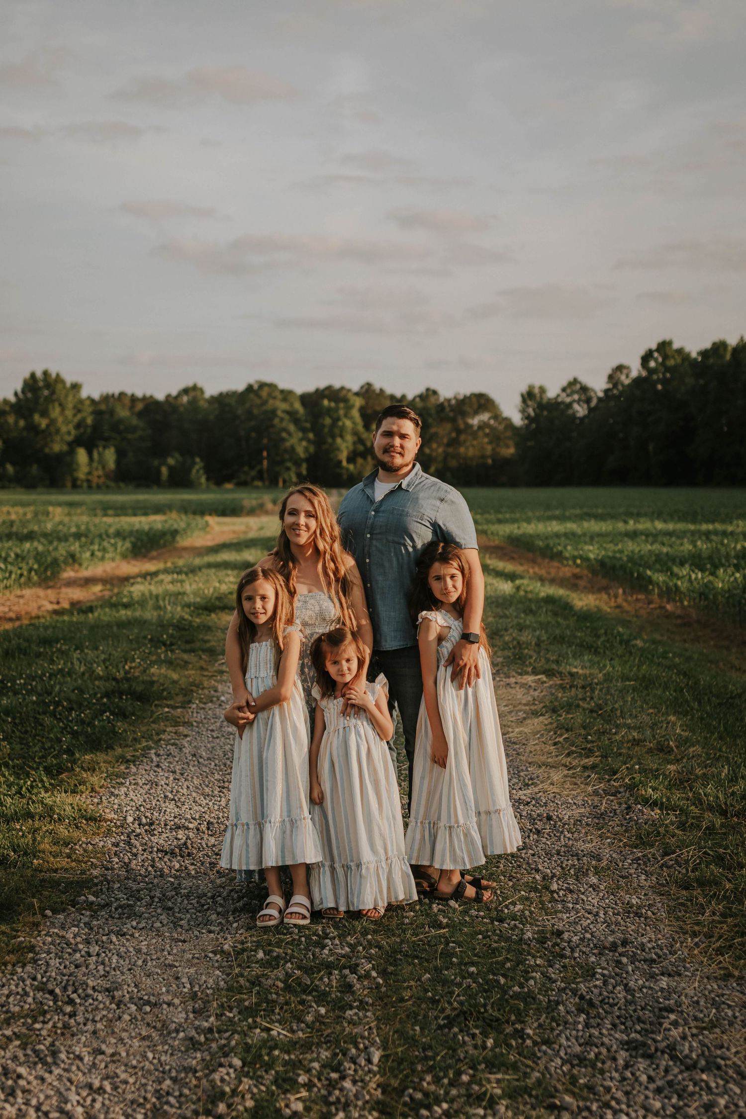 Group of children in light blue dresses pose together on a gravel path at sunset.