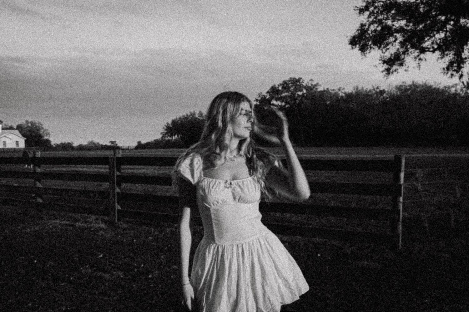 A black and white wedding photo shows a bride in a lace dress twirling in a rustic field at sunset.