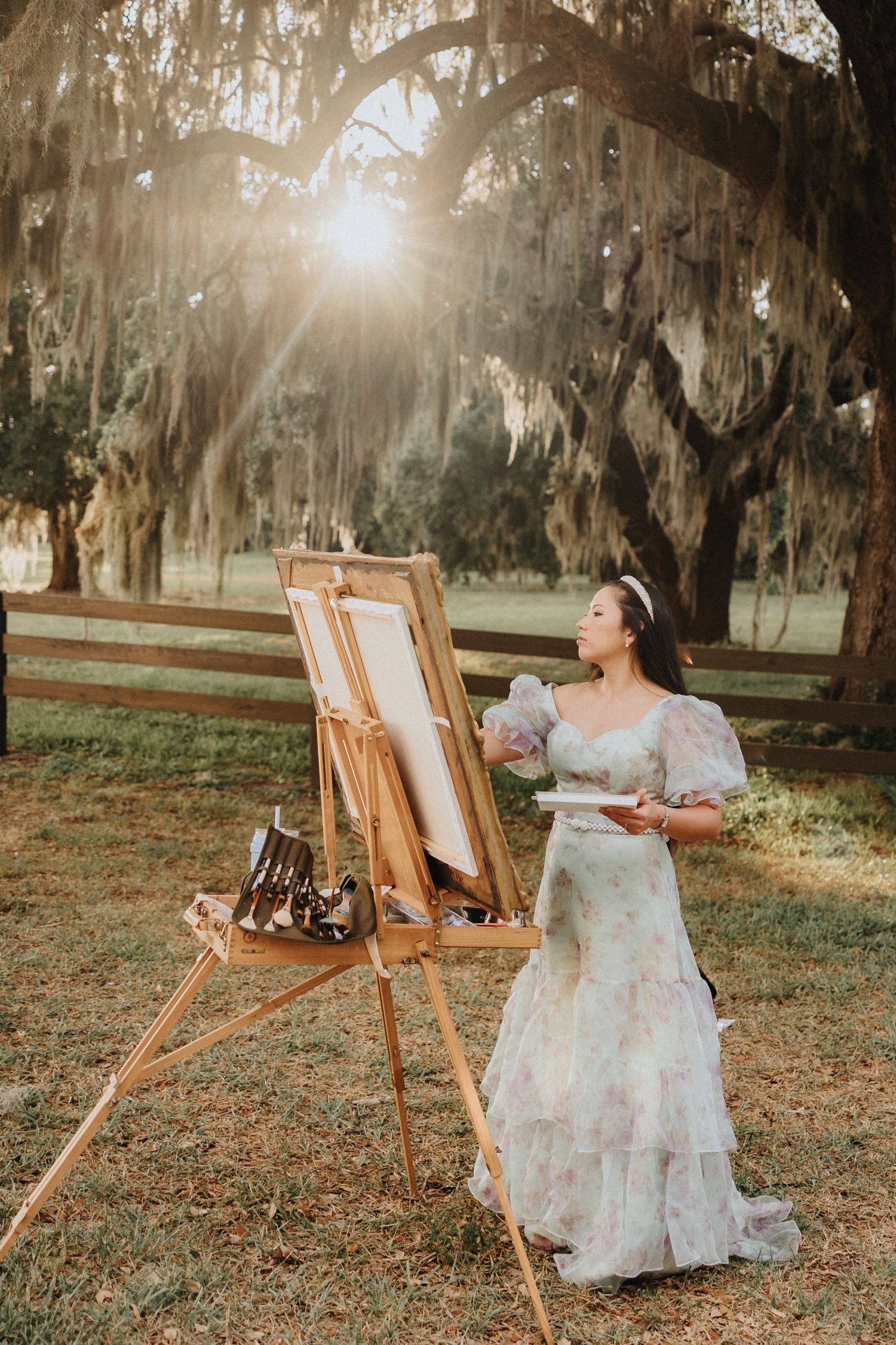 Artistic outdoor photoshoot in a dreamy Spanish moss-draped setting with wooden easels and soft sunlight filtering through trees.