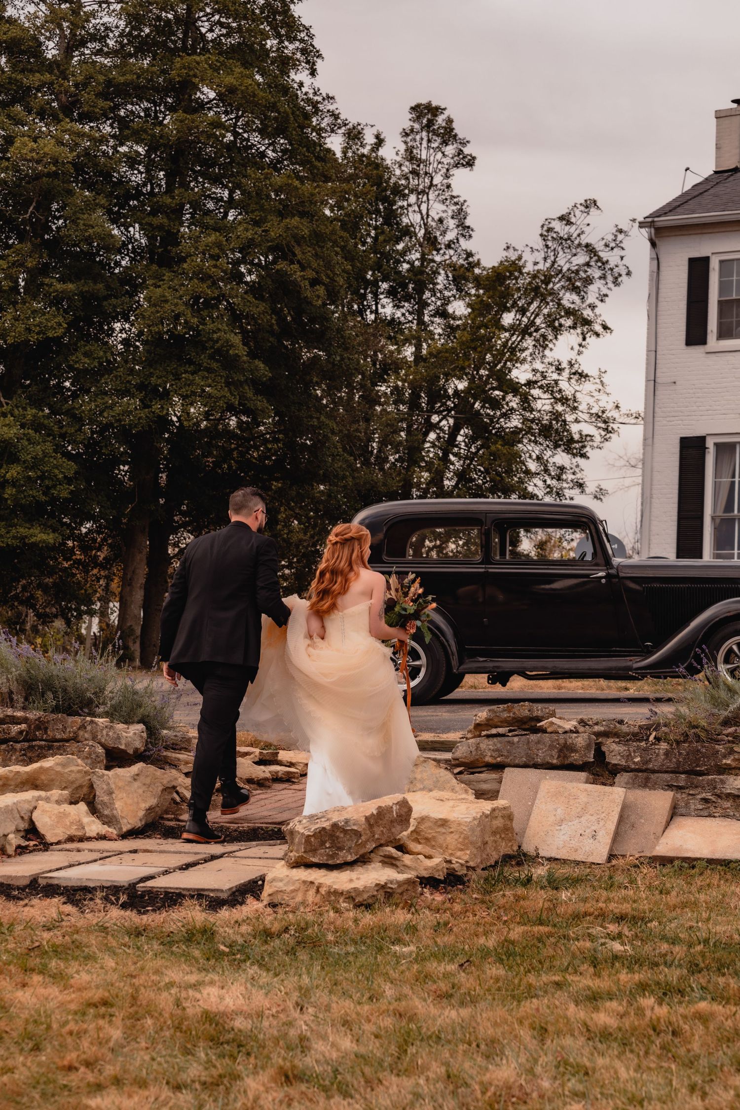Outdoor wedding scene with classic car and white house in autumn setting.