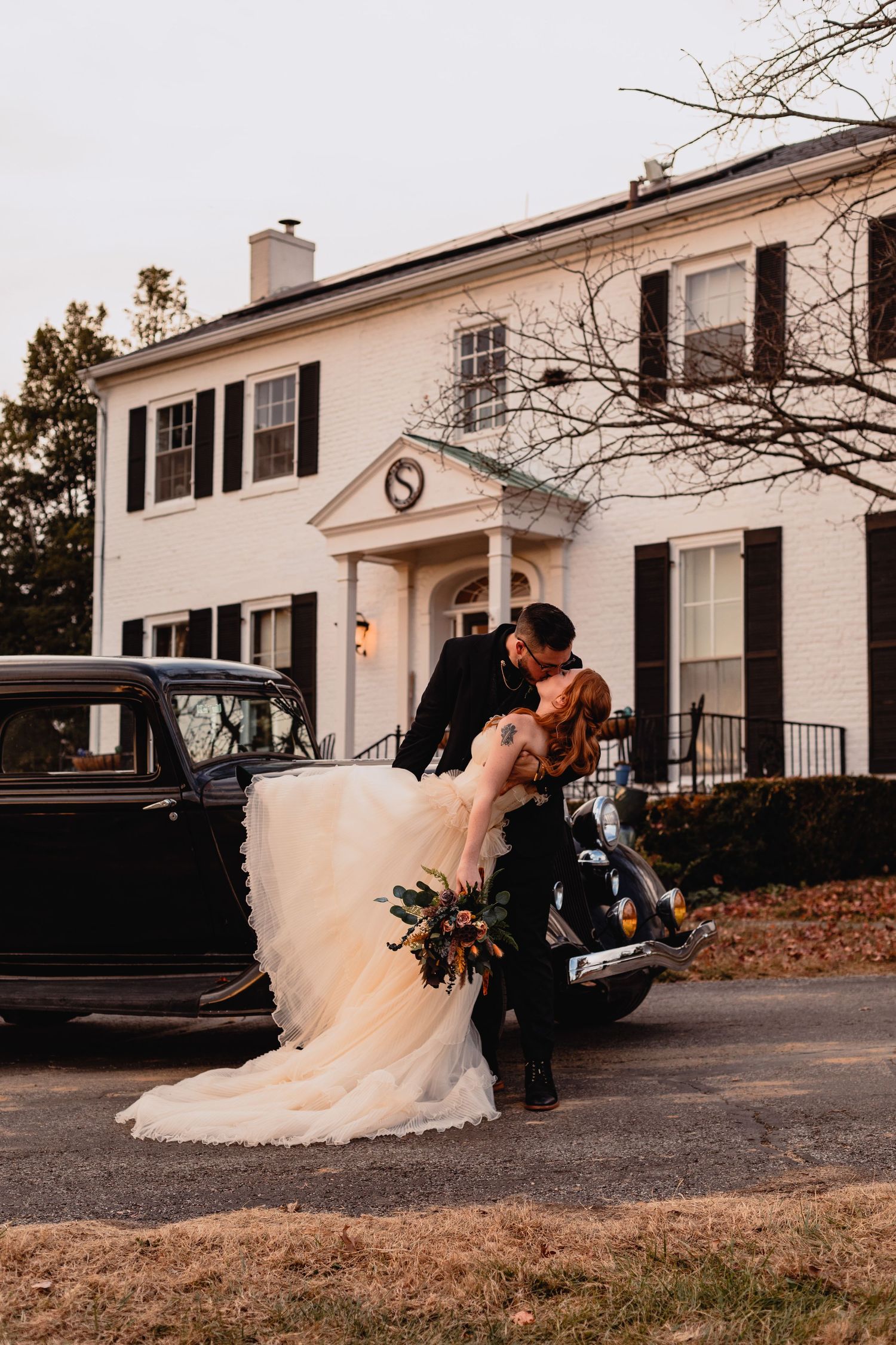 Romantic wedding moment captured outside classic white colonial house.