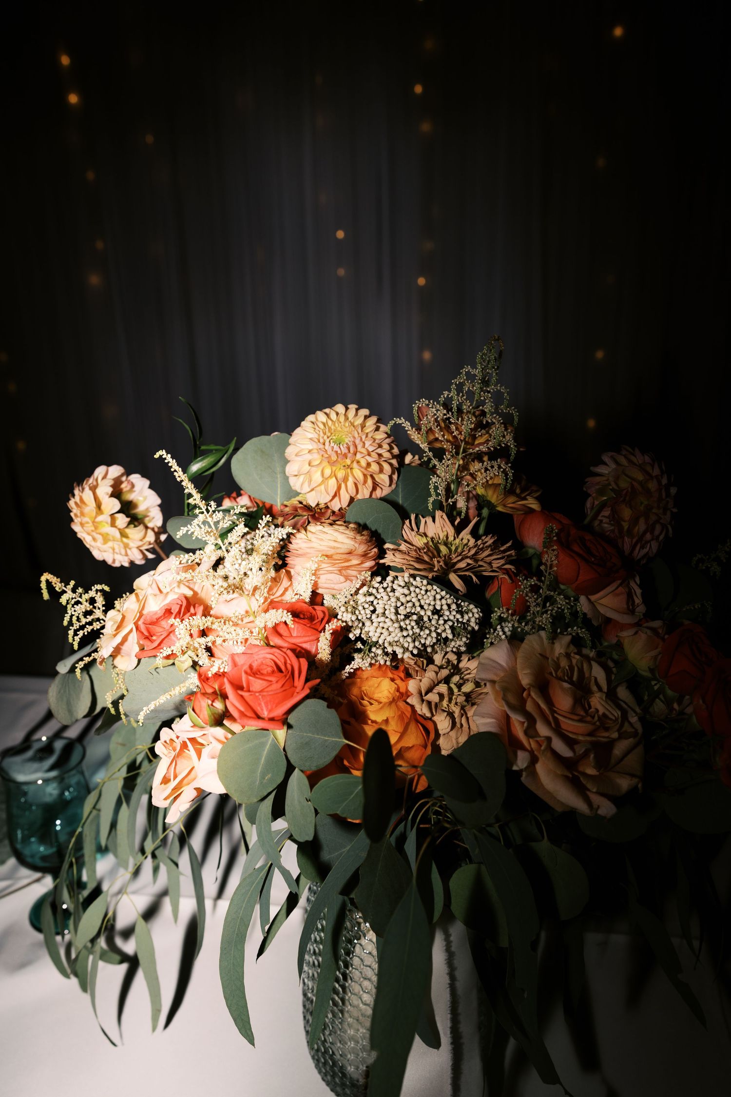 Elegant floral arrangement featuring peach dahlias, roses, and eucalyptus leaves against a dark moody background.