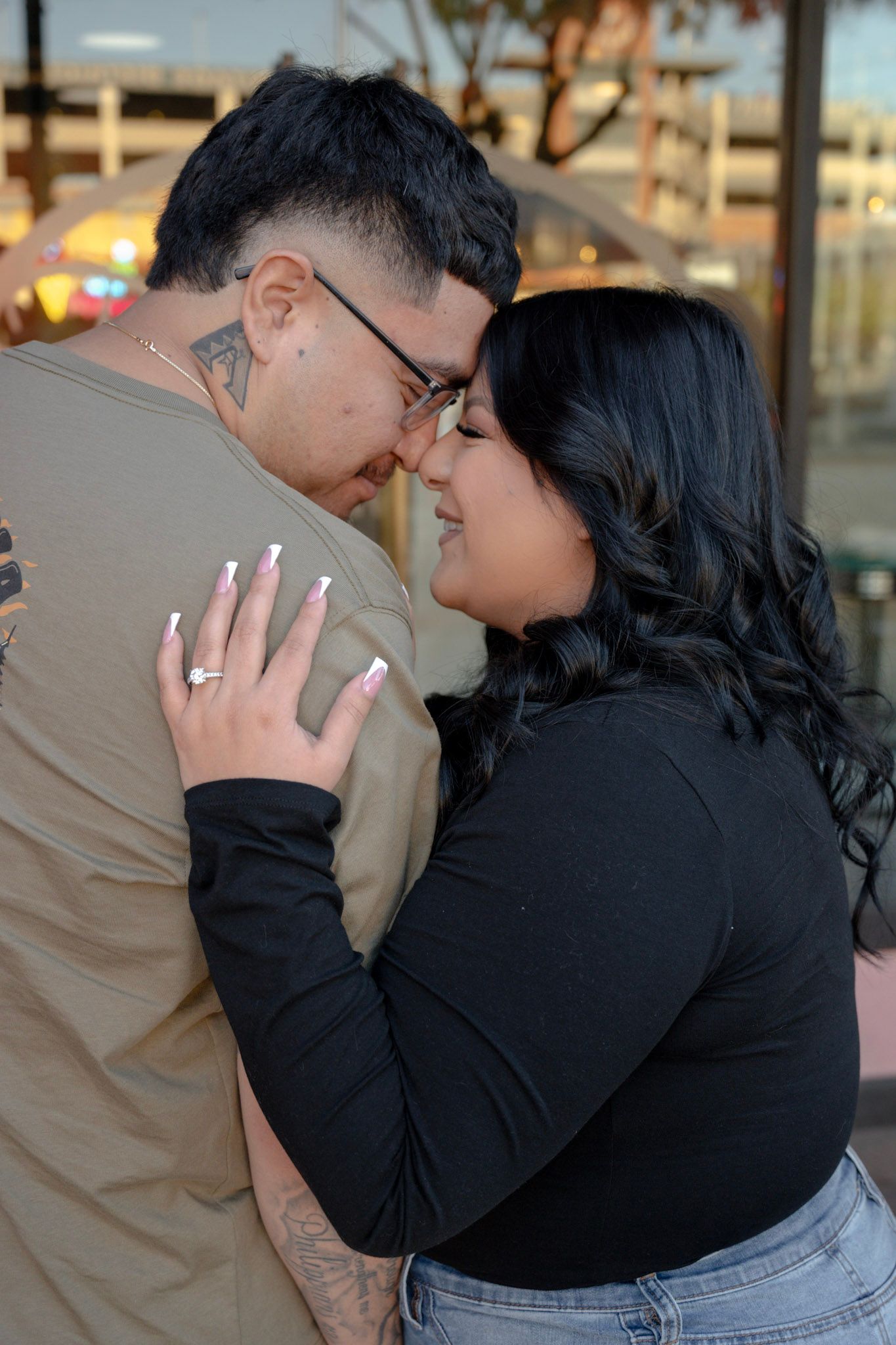 Couple shares an intimate forehead-to-forehead embrace outdoors, woman displaying engagement ring.