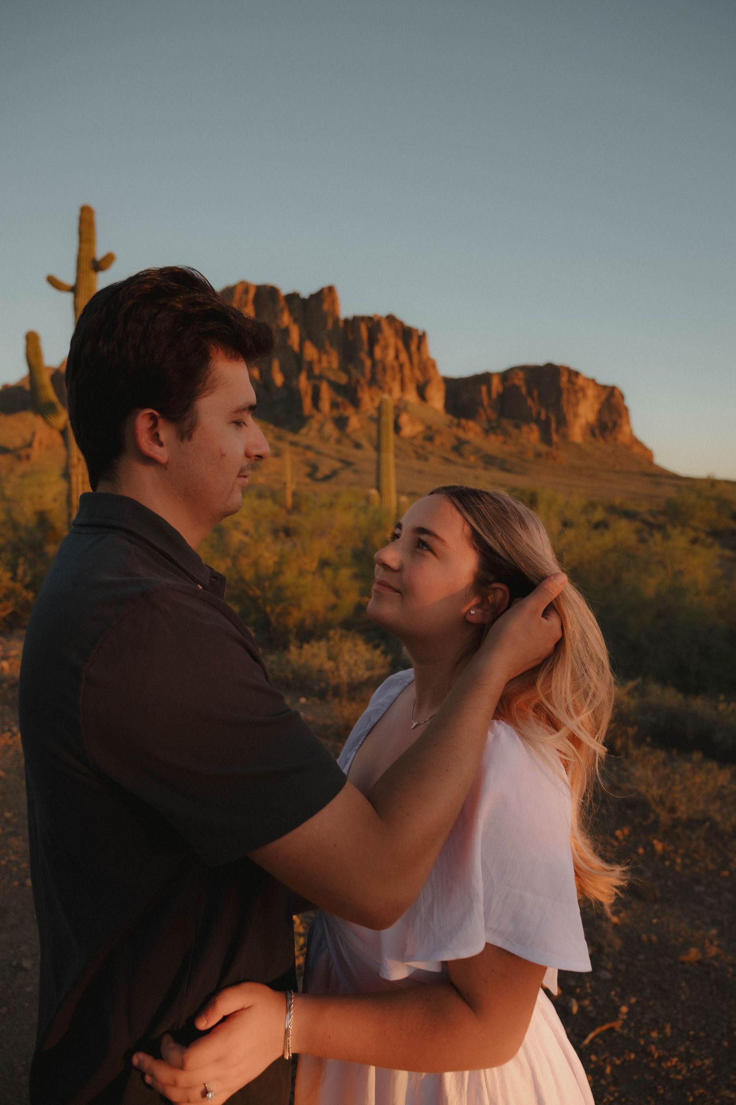 Couple embracing at golden hour in Arizona desert with saguaro cacti and Superstition Mountains backdrop.