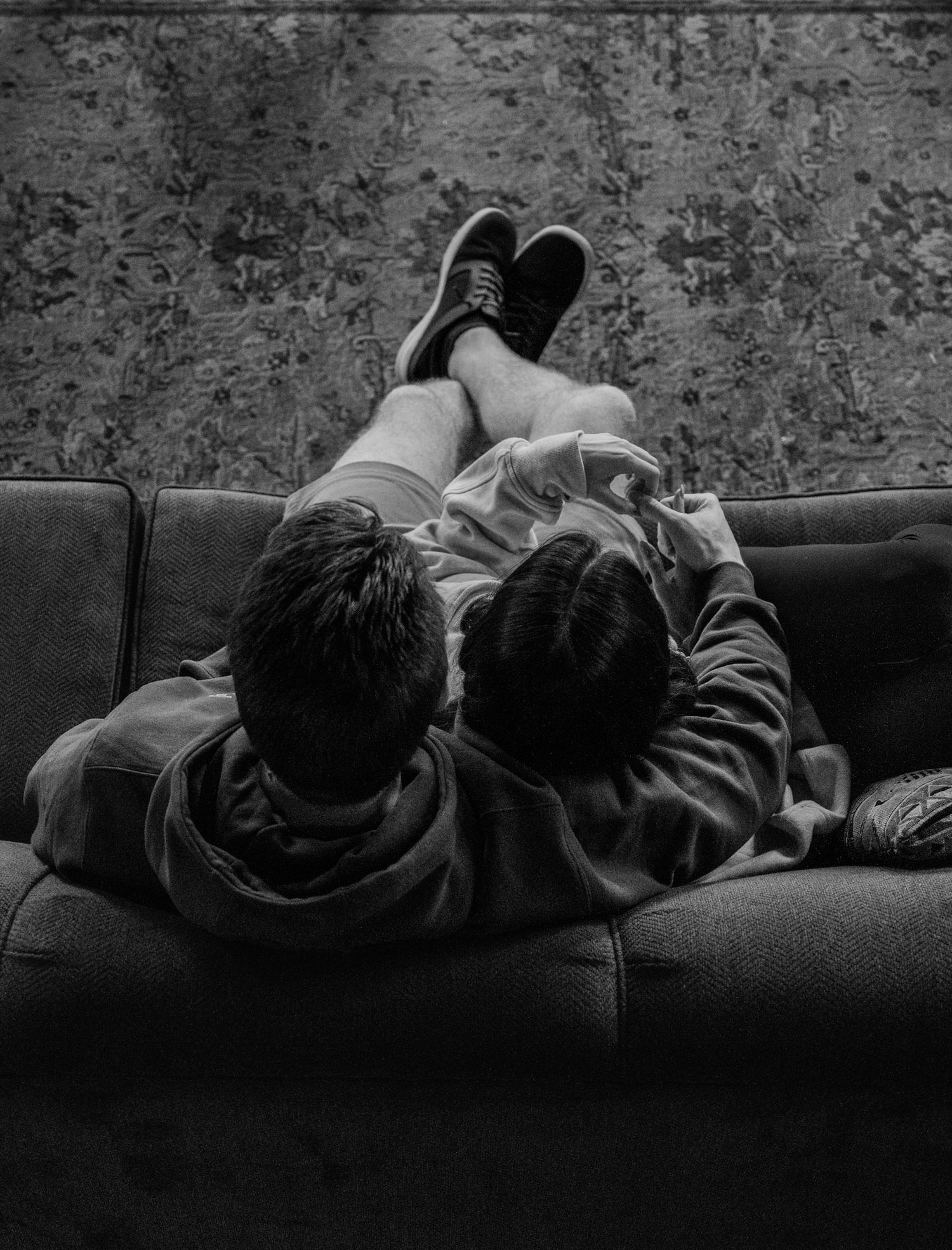 Black and white overhead photo of two children lying on a couch looking at a device together.