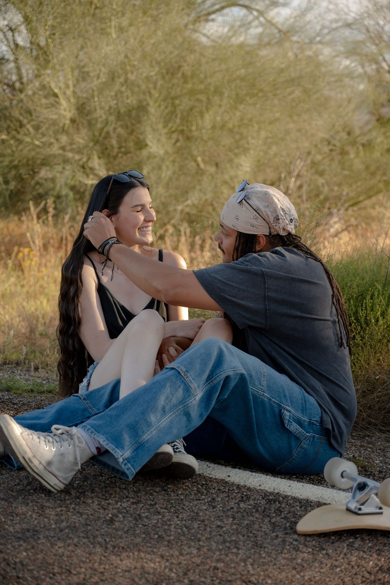 Couple sits together on a gravel path laughing in warm afternoon light with desert shrubs behind.