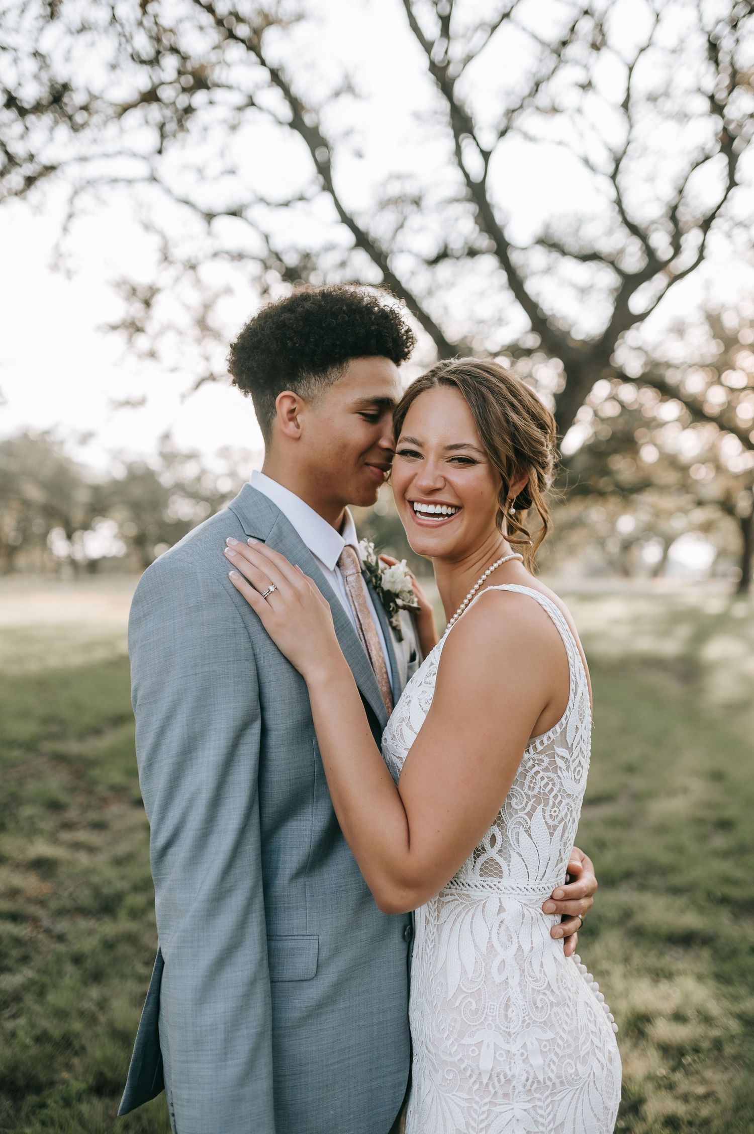 Joyful wedding couple embrace outdoors under branching tree.