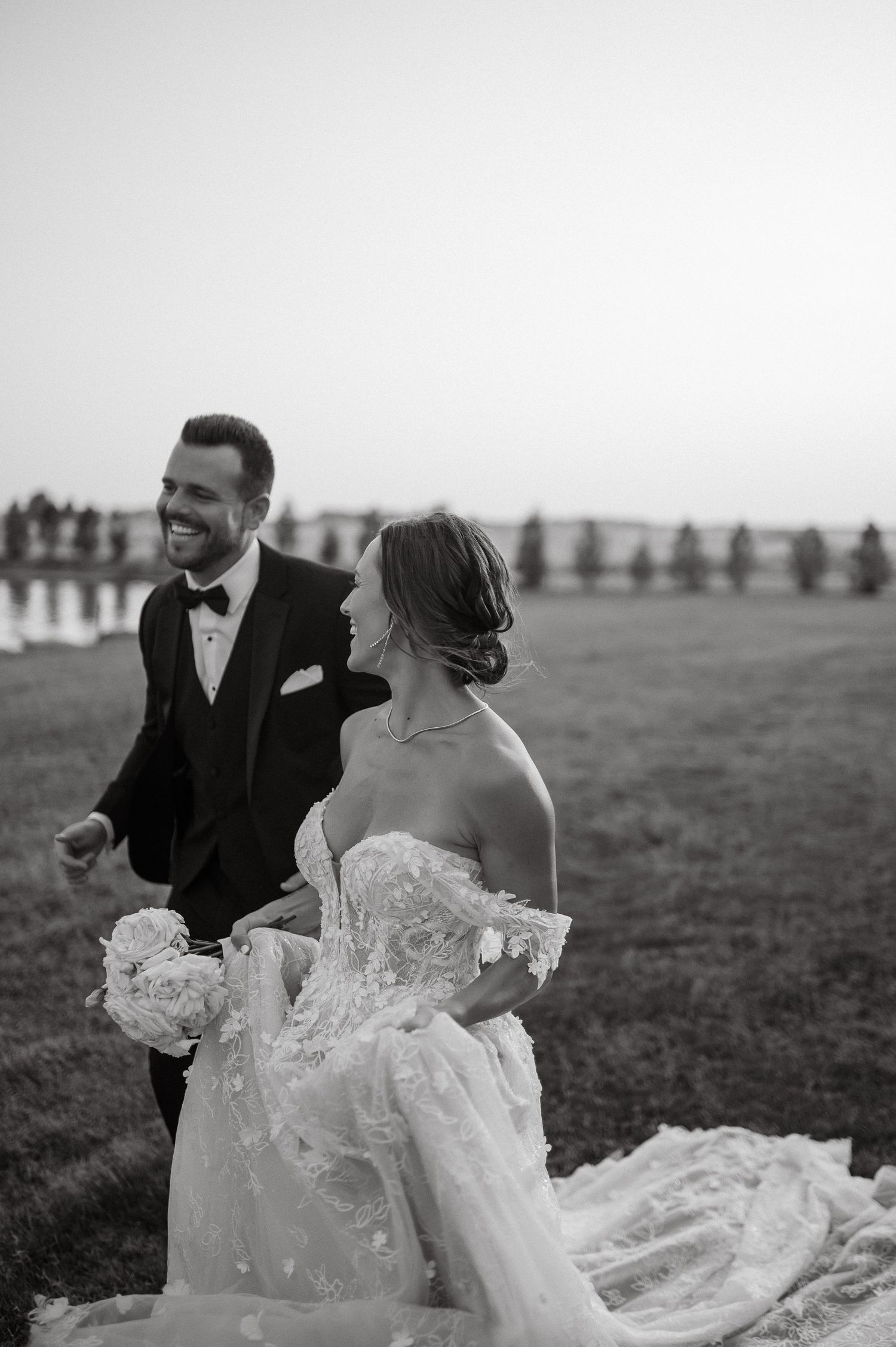 A joyful couple in wedding attire share a candid moment outdoors during their black and white wedding photoshoot.