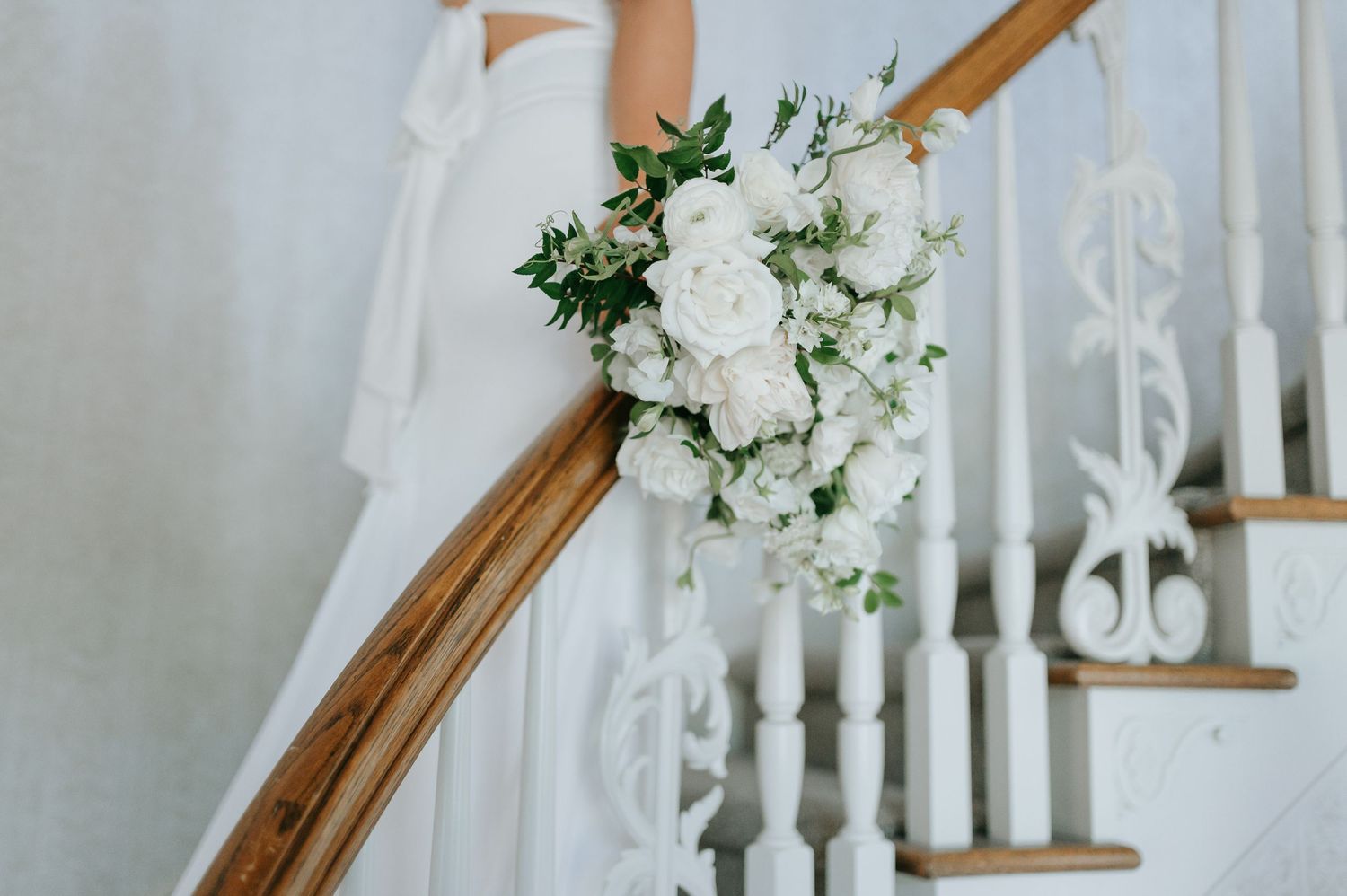 White floral bouquet with greenery rests on a wooden staircase banister. Gorgeous Estate Wedding in Lubbock, Texas.