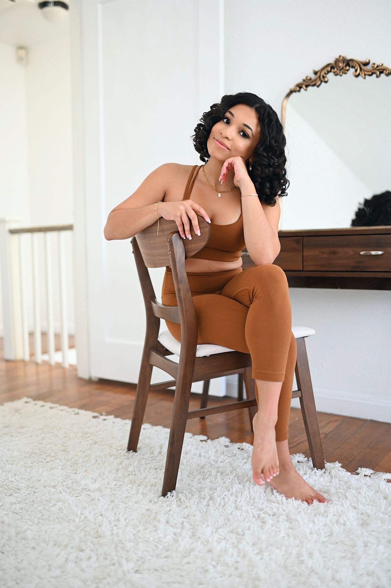 Woman in brown matching sports bra and leggings set sitting on wooden chair indoors.