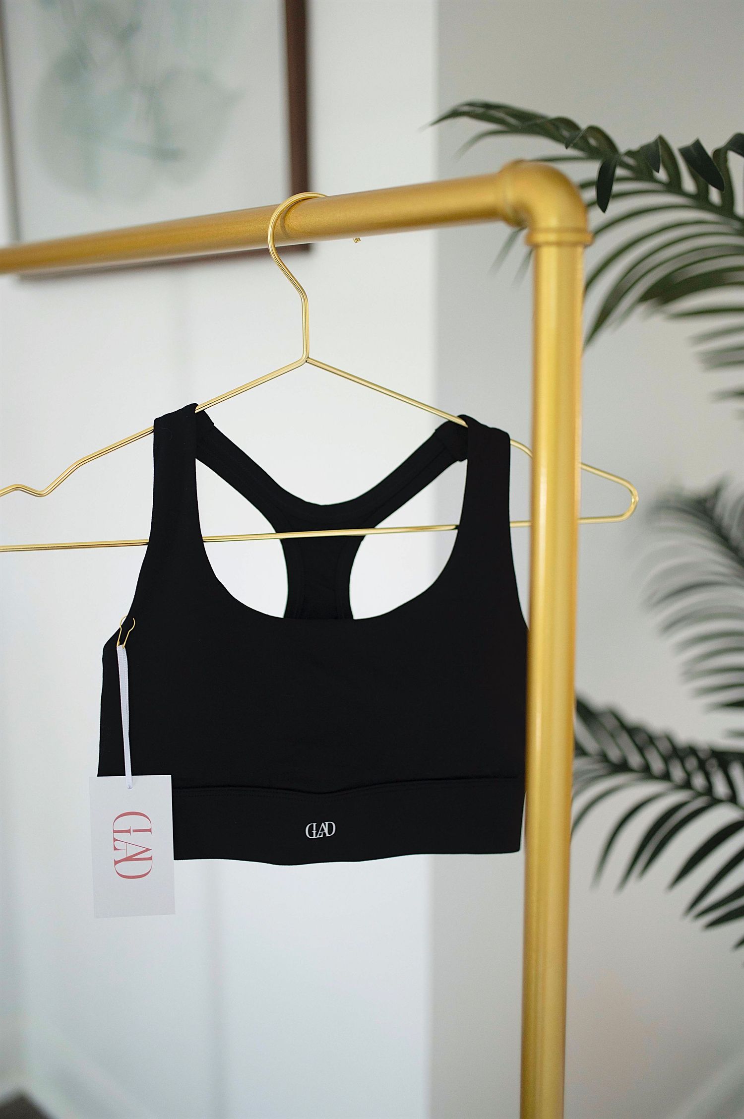 Black racerback sports bra with logo tag hanging on gold clothing rack.