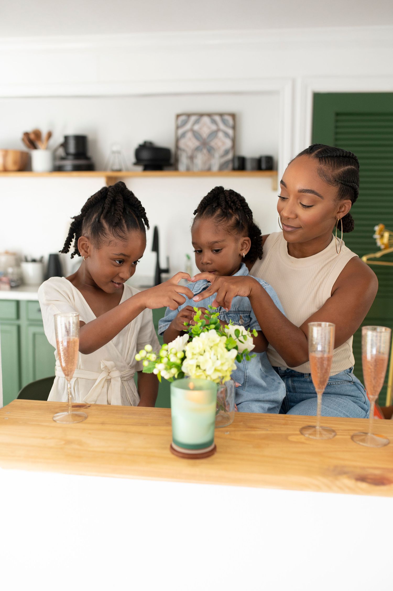 A Black mother and two daughters arrange flowers at a kitchen counter.