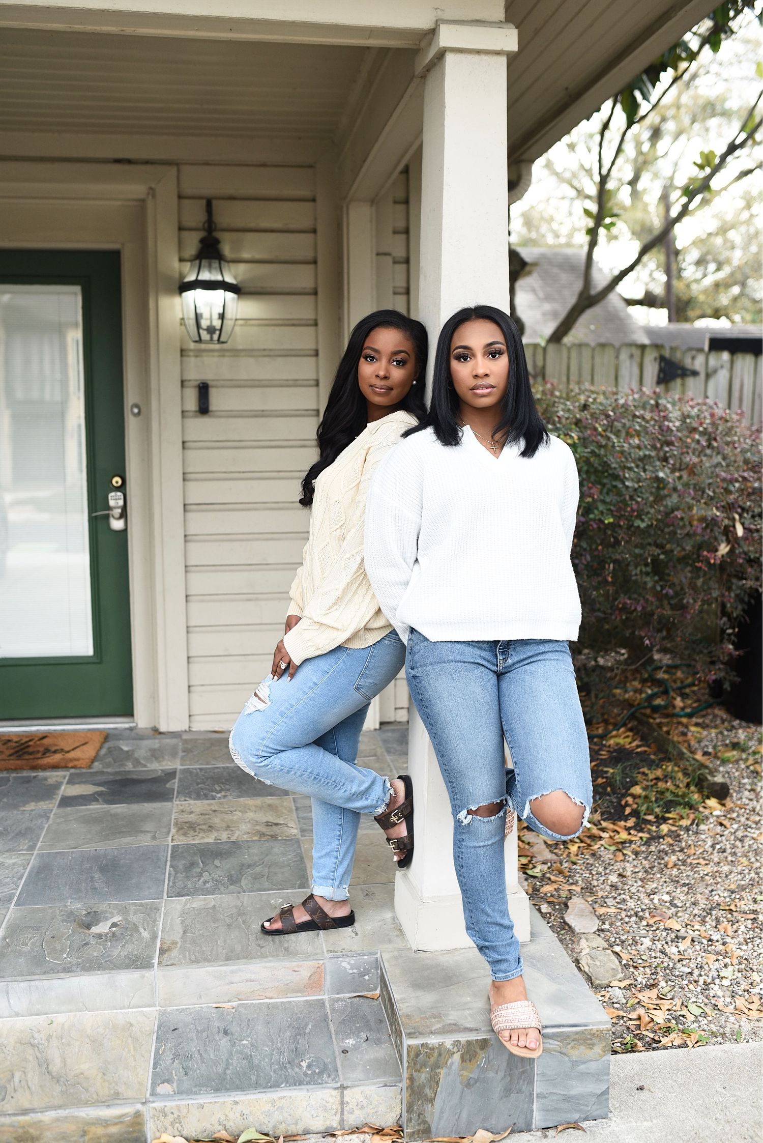 Two young women in jeans and white tops posing on home front porch steps.