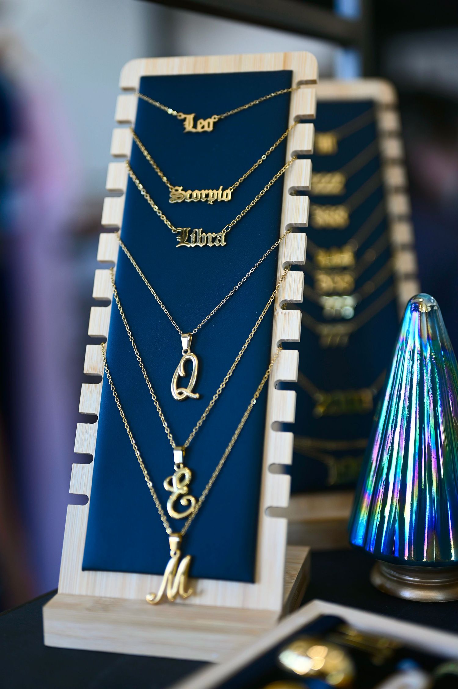 Gold zodiac sign and initial letter necklaces displayed on tiered navy velvet jewelry stand.