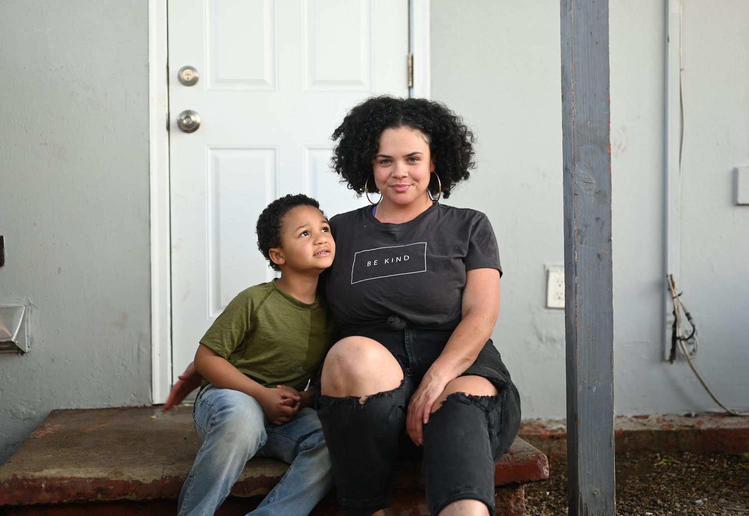 Black mother and young son sitting together on front porch steps, smiling warmly.