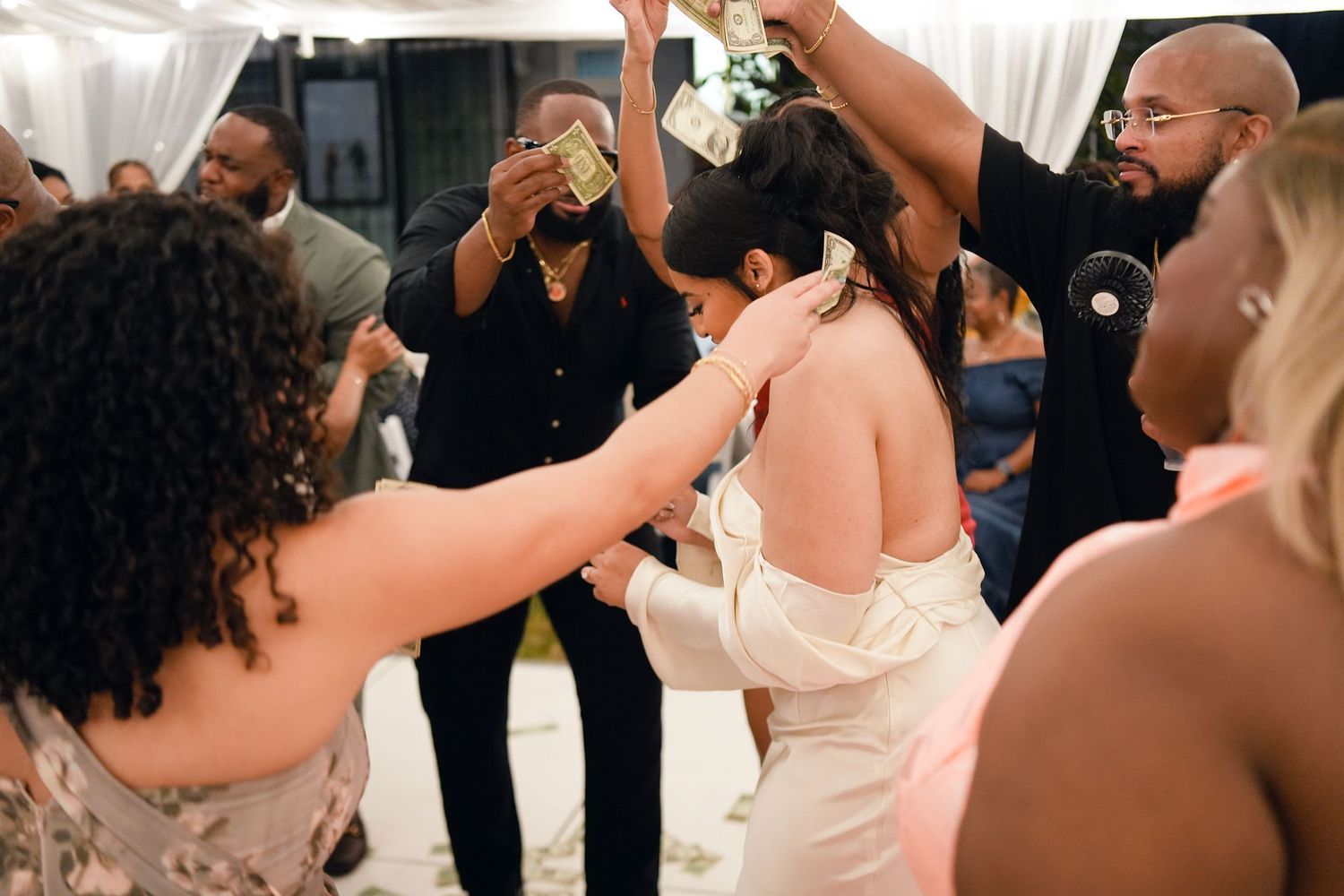 Bride in white backless gown dancing joyfully with guests at a lively wedding reception.