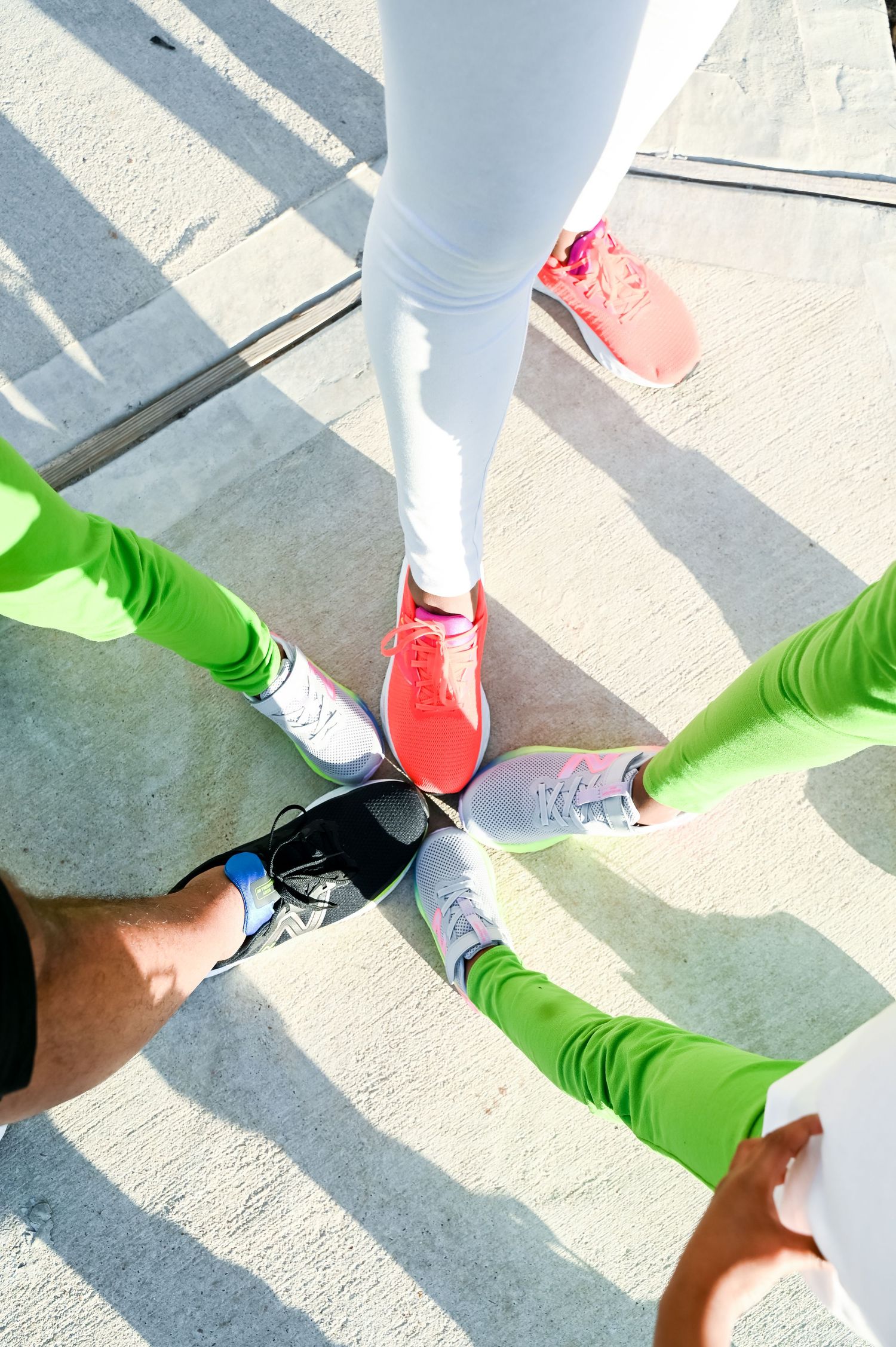 Top view of four people in green and white leggings wearing colorful athletic sneakers in a circle.