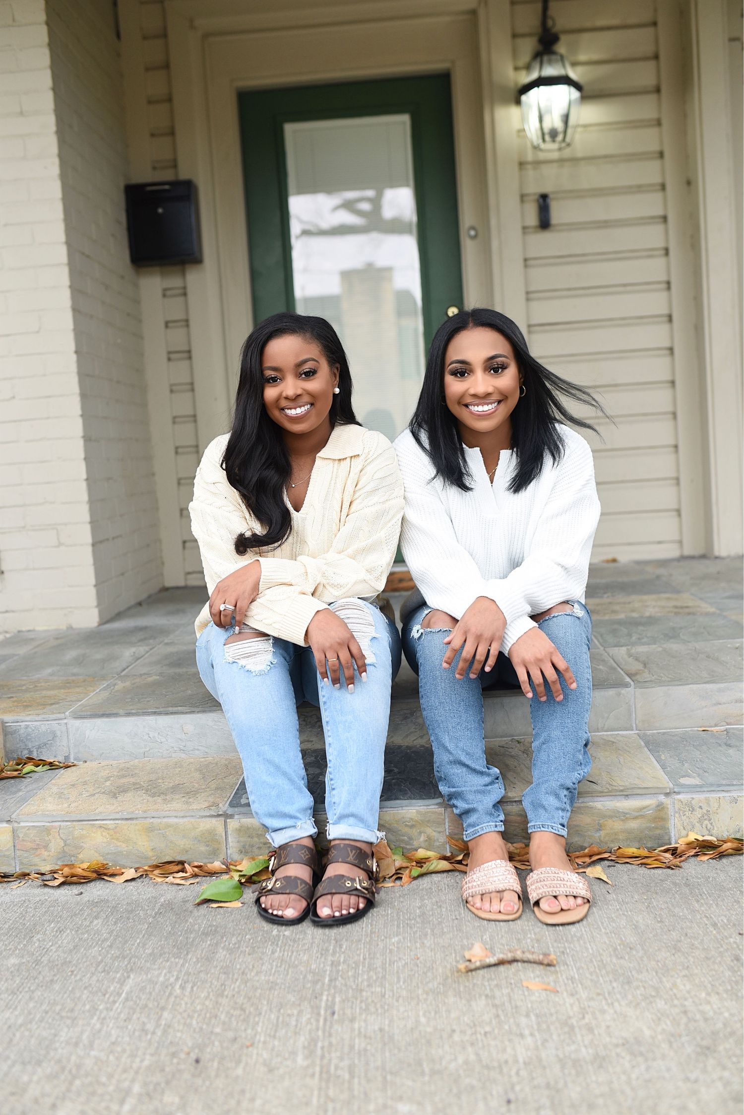 Two smiling women in casual white tops and jeans sitting on front porch steps.
