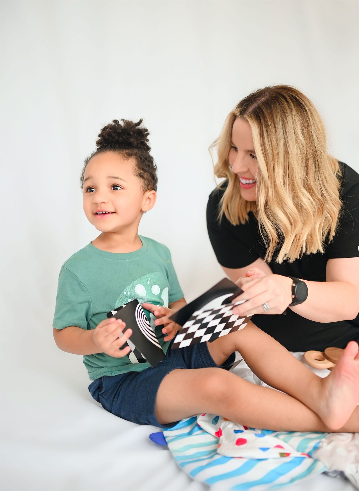 Blonde woman and young boy smiling while reading black and white book together on white background.