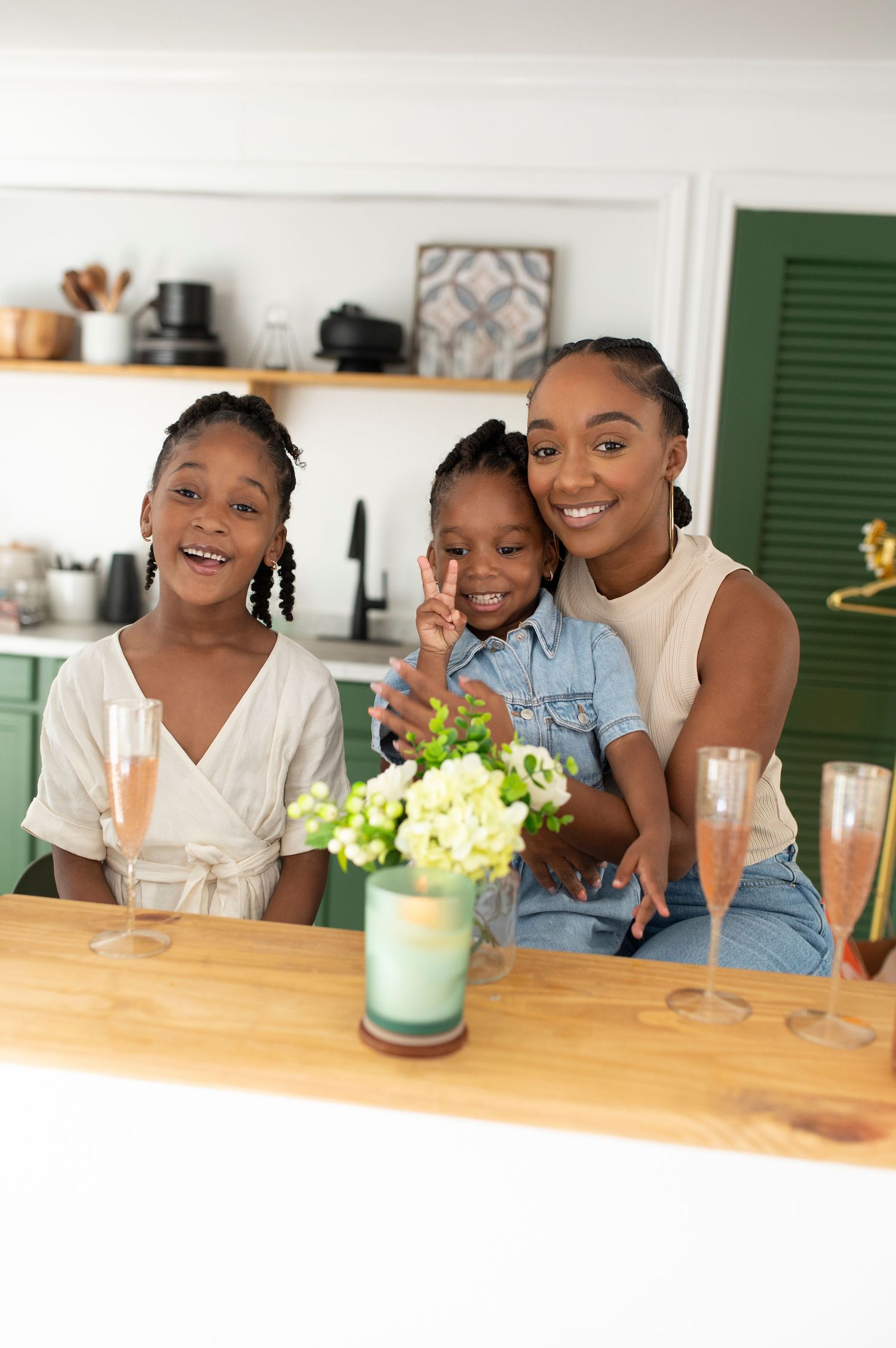 A smiling Black mother poses with her two daughters in a modern kitchen.