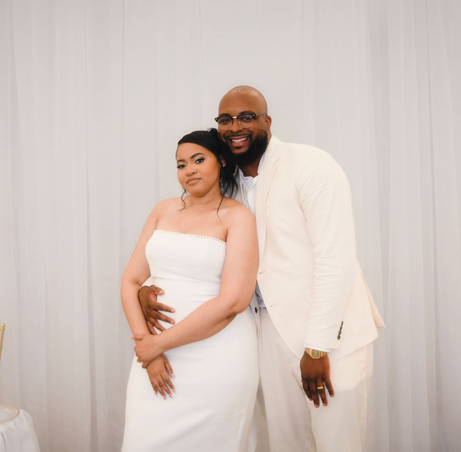 Couple posing together at a wedding, bride in white strapless gown and groom in cream suit.
