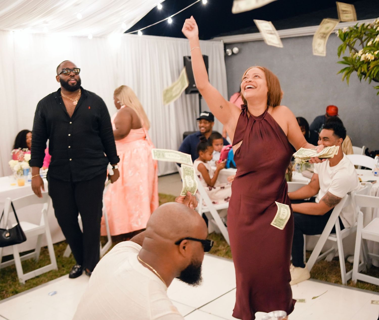 Guests celebrating at an outdoor evening party with money being tossed in the air.
