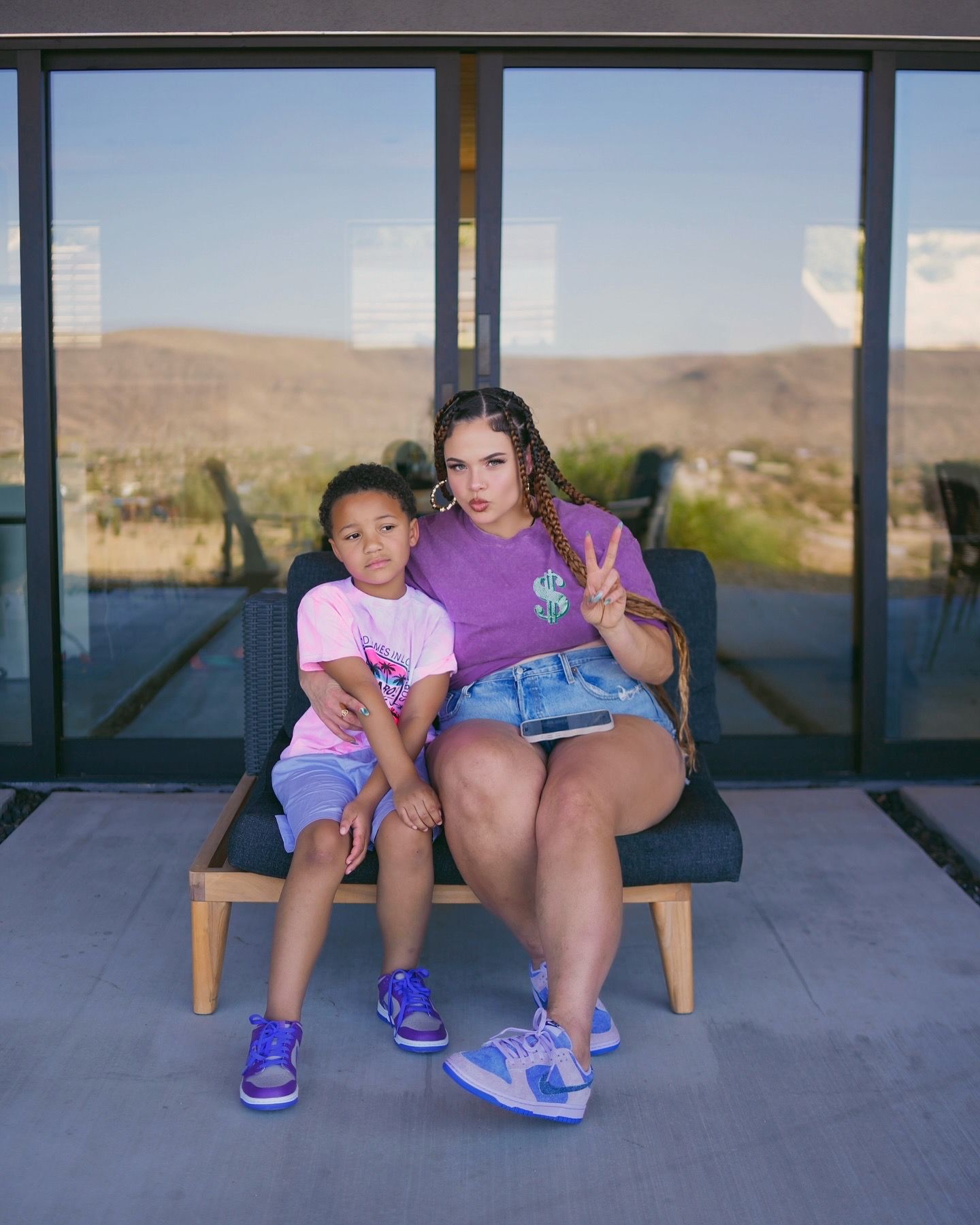 Woman and child in coordinating purple and pink outfits posing on chair with desert landscape background.