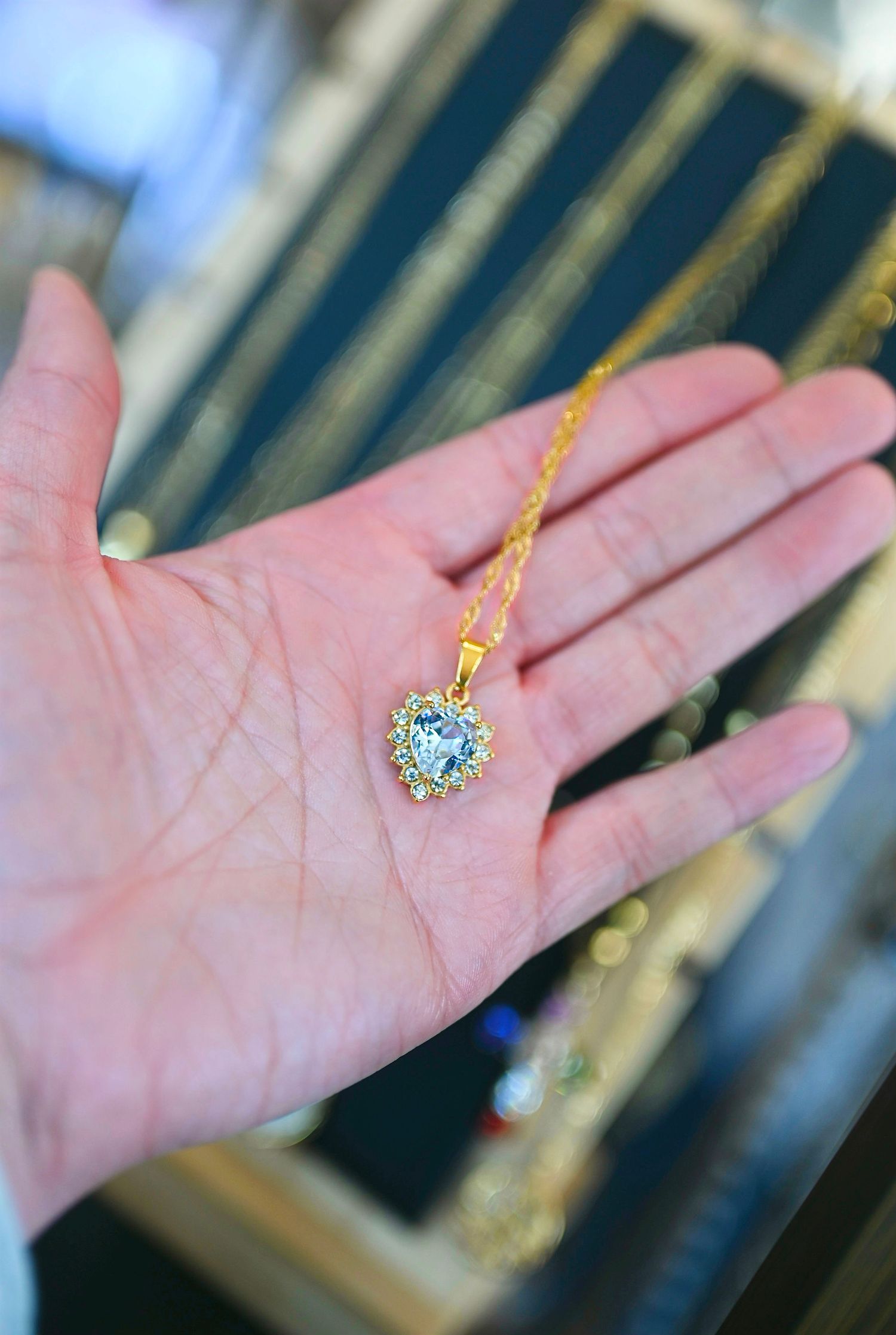 Hand holding a gold heart-shaped pendant necklace with crystal halo on a delicate chain.