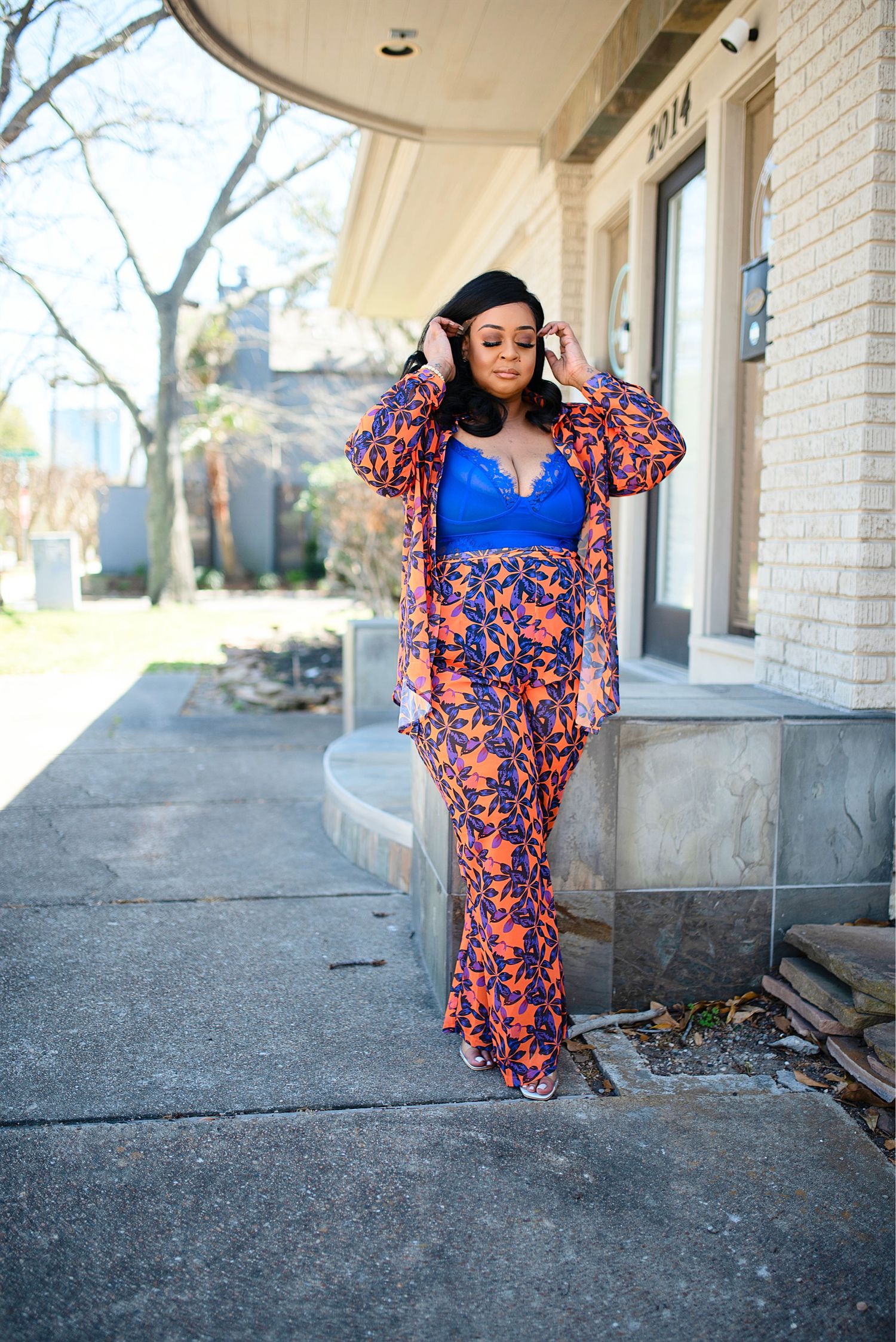 Woman wearing a blue crop top with orange floral wide-leg pants and kimono on a sunny sidewalk.