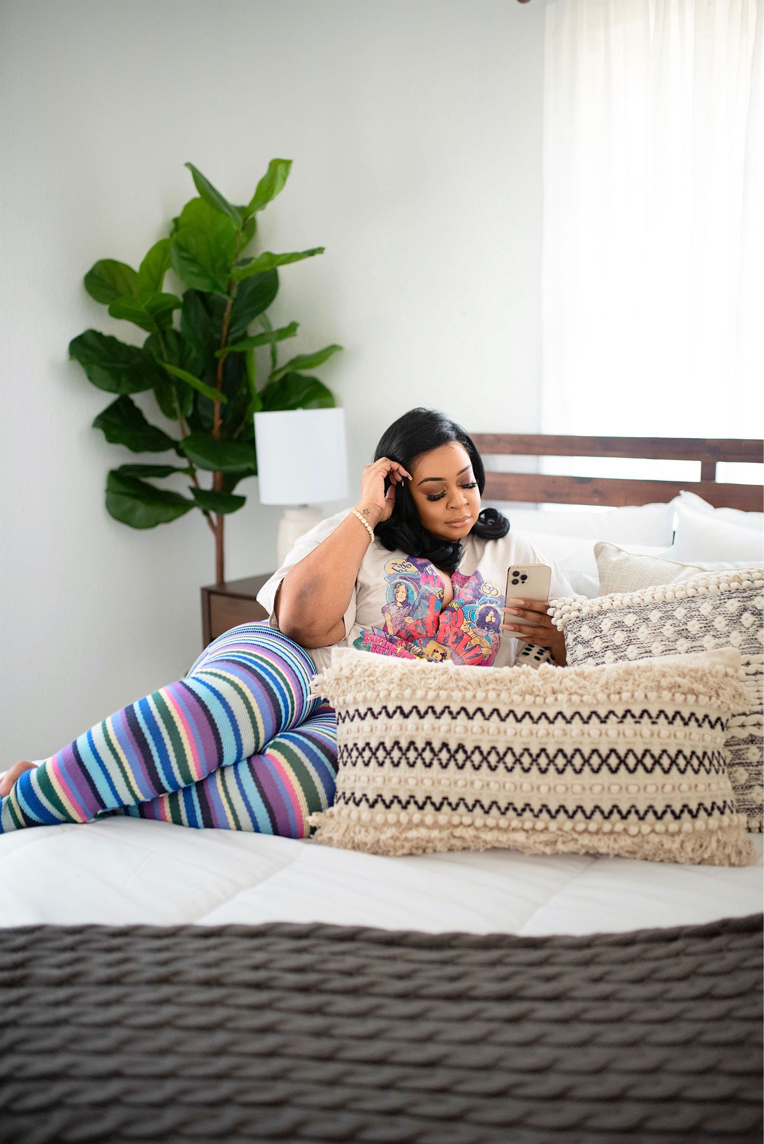 Woman in multicolor striped leggings relaxing on a bed while using her smartphone indoors.