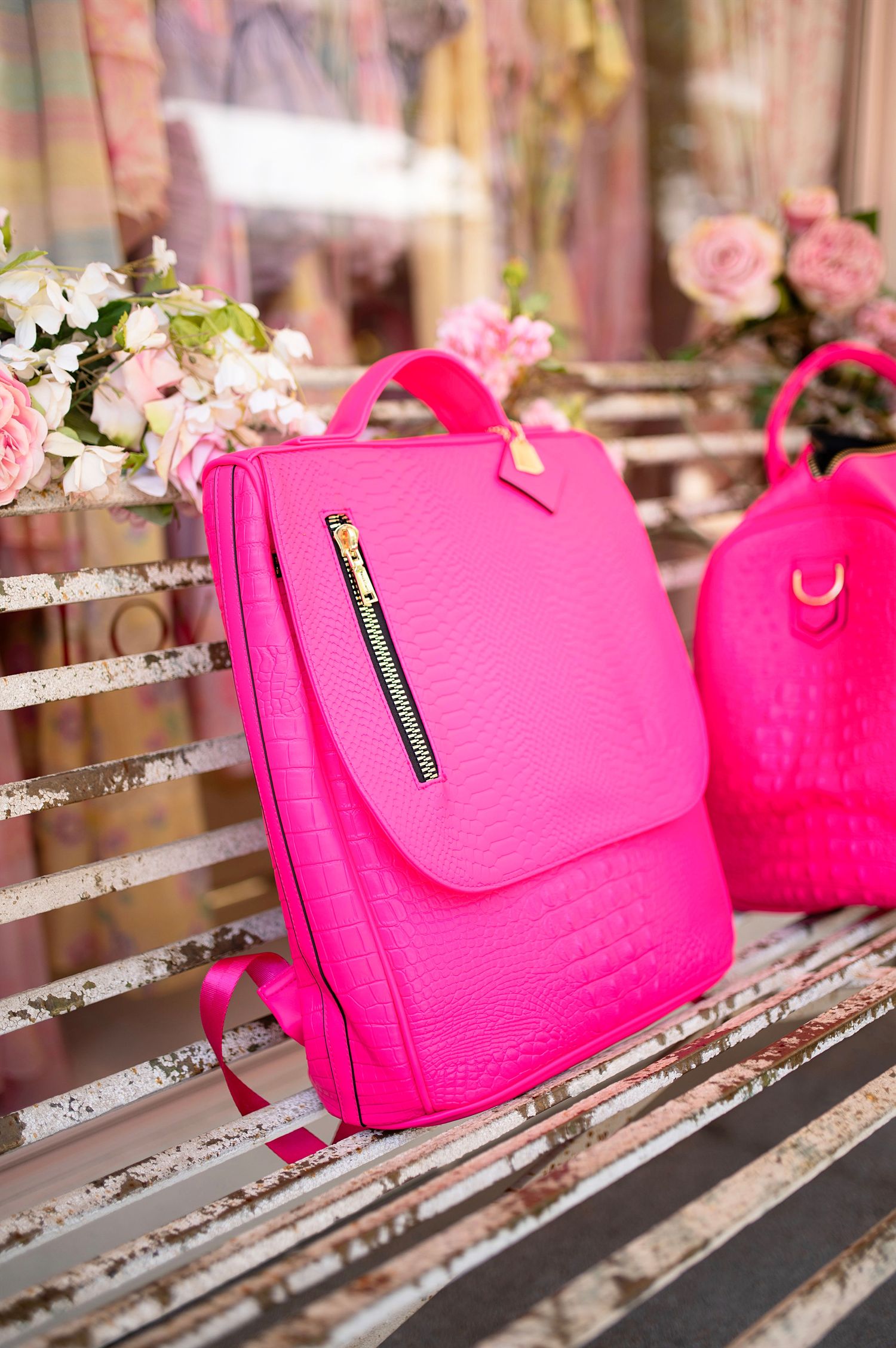Bright pink textured leather backpack with gold zipper displayed on vintage white bench with roses.