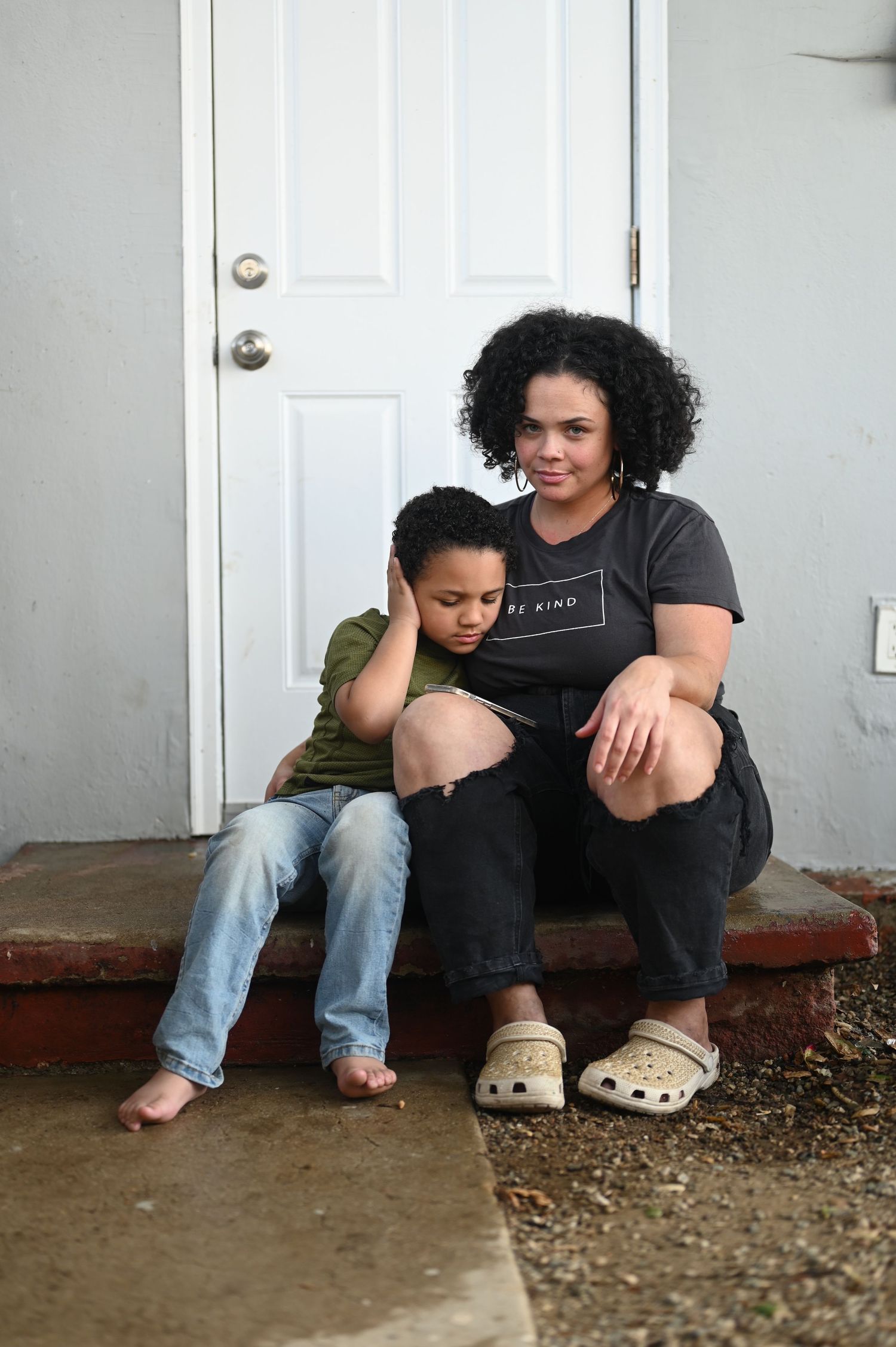 Mother and young son sit together on front porch steps in casual clothing.