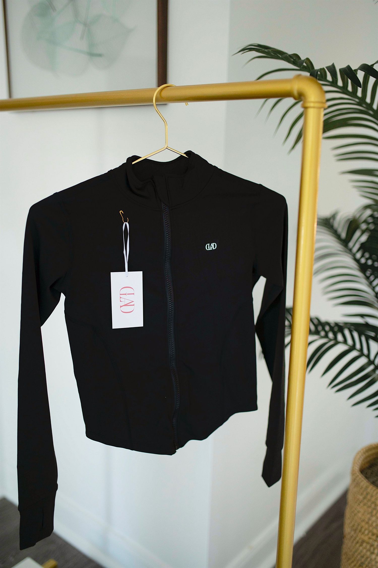 Black zip-up athletic jacket with logo tag displayed on gold clothing rack.