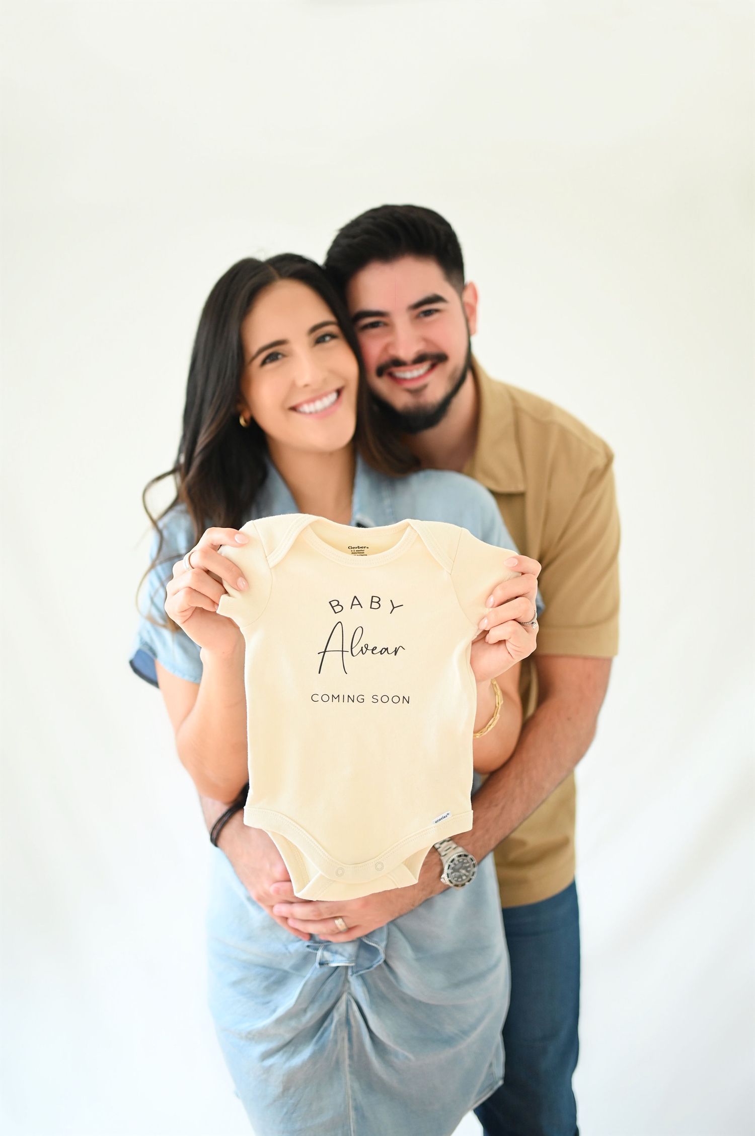 Smiling couple holding Baby Alcazar coming soon onesie for pregnancy announcement.