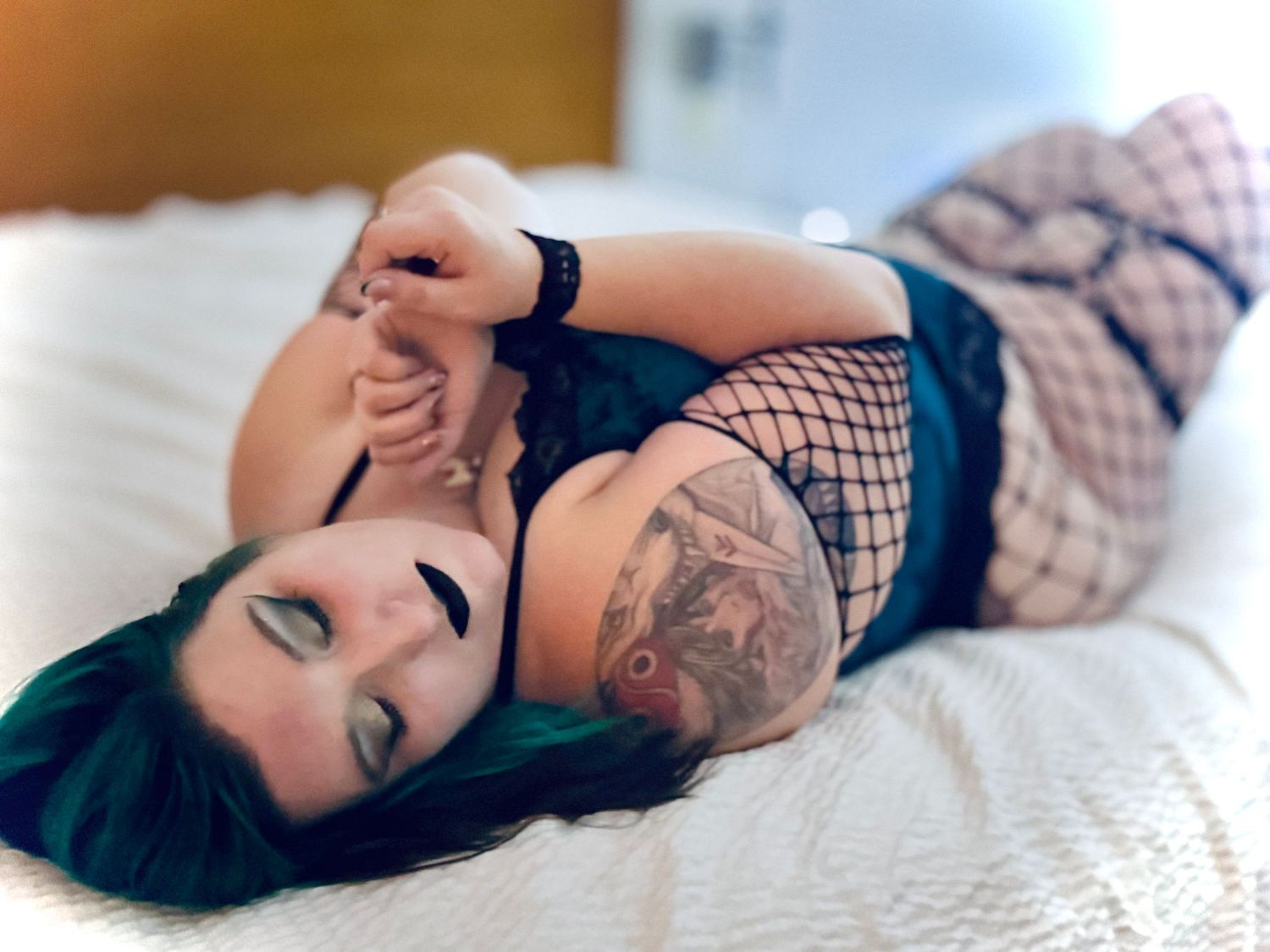 Woman with dark hair wearing lingerie poses seductively on white bedding in boudoir photo series.