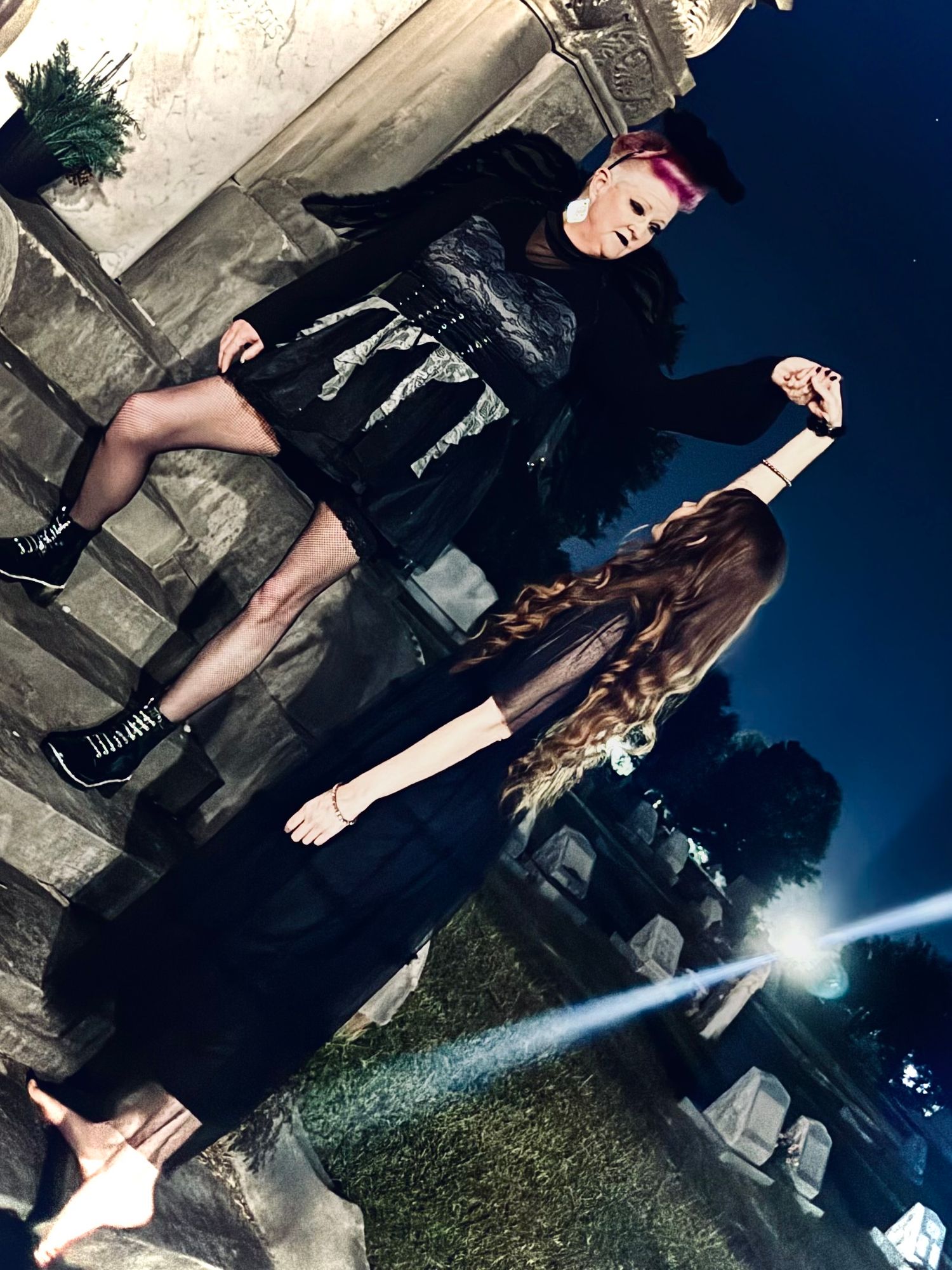 Two women, in dark clothing poses against a stone wall backdrop in a series of moody artistic photographs.