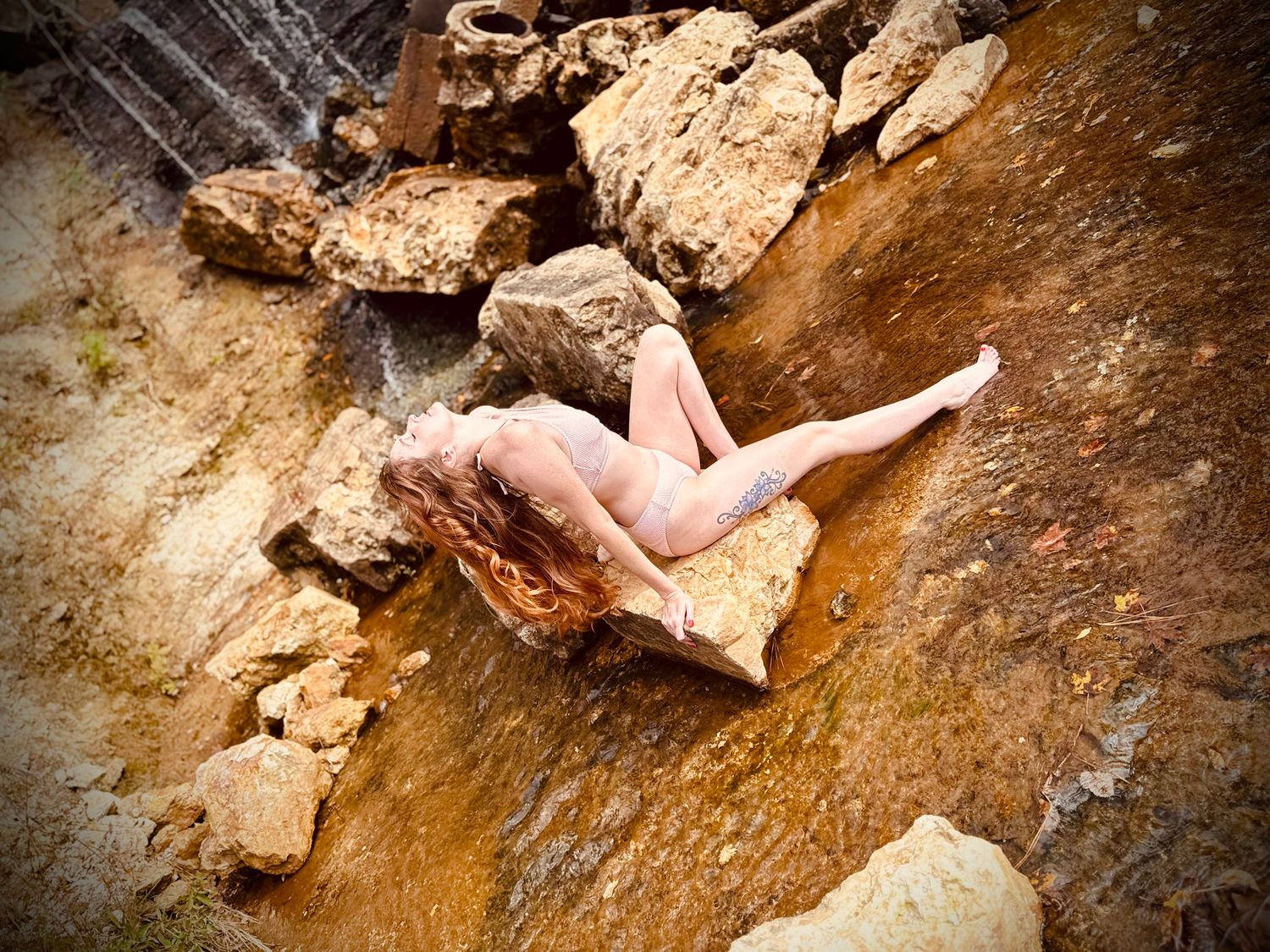 Stunny woman relaxing on a rock as the waterfall flows behind her.