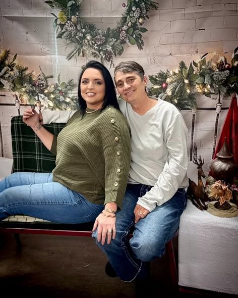 A couple sits casually together on a bench in a cozy room decorated with plants and white brick walls.