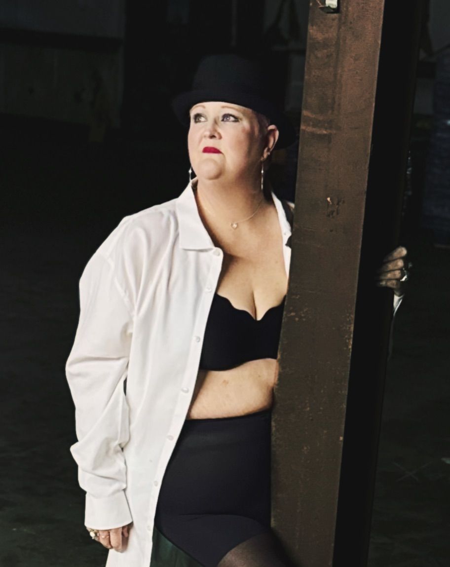 A figure in a white jacket and black dress poses dramatically against a dark background. Showing off her boldness.