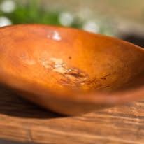 Closeup macro shot of a rustic wooden bowl's edge with warm lighting highlighting its natural grain texture and curves.