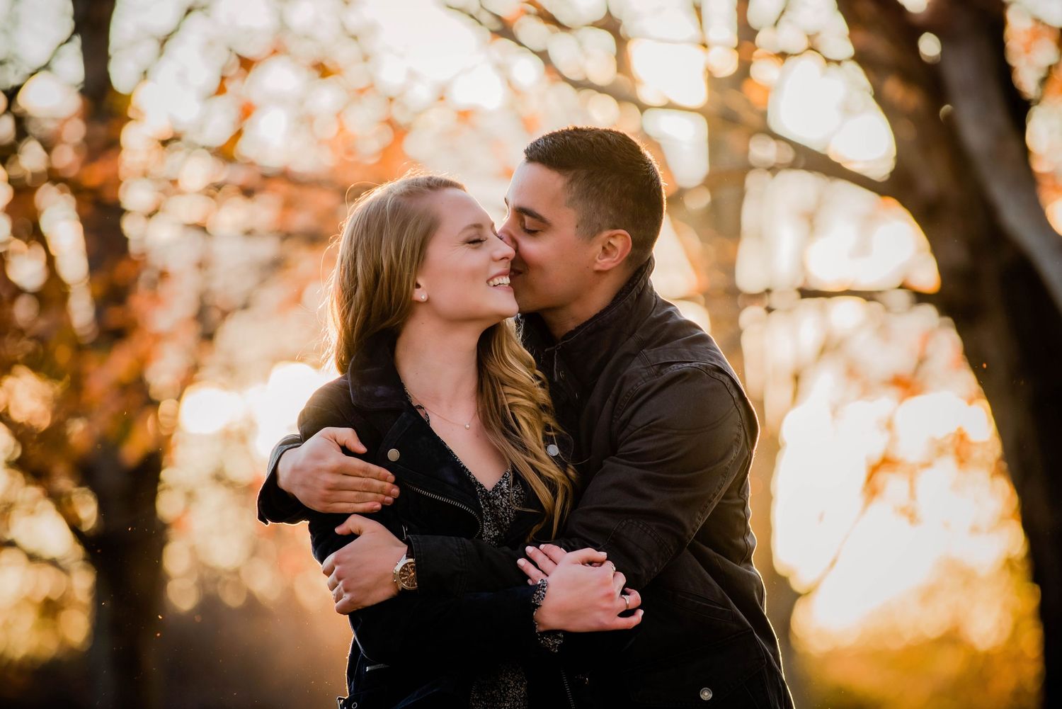 A romantic couple embraces during golden hour sunset with autumn foliage in the background.