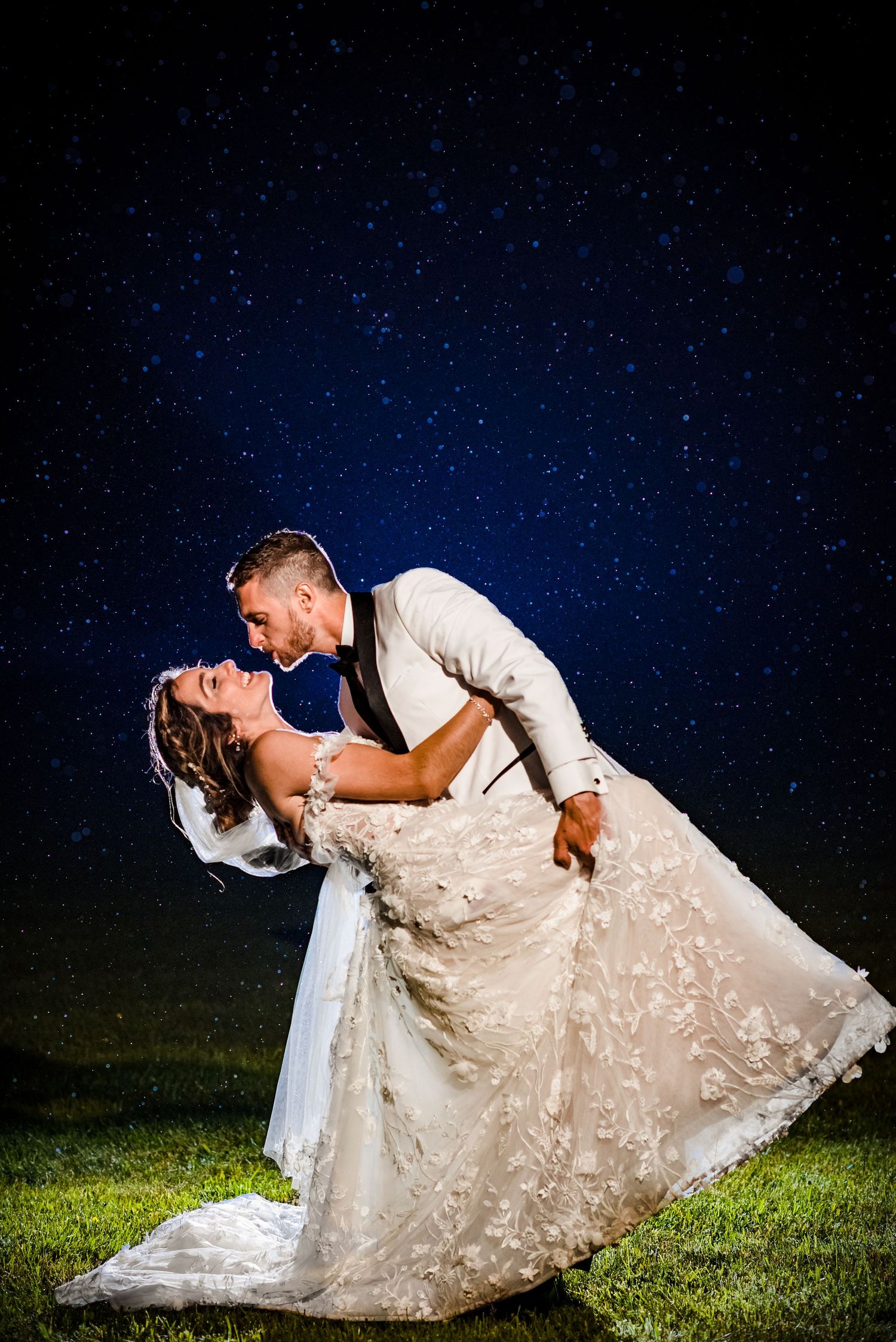 Bride and groom share a romantic dip kiss under a stunning starry night sky on their wedding day.