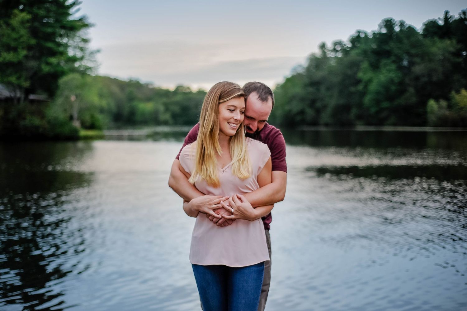 Romantic lakeside moment captured during golden hour with trees in background, photographed by a Rhode Island photographer.