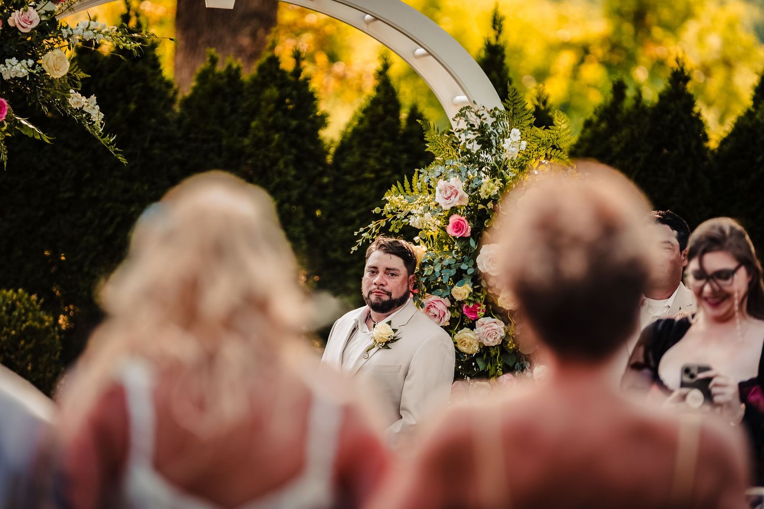 Wedding ceremony under a floral arch with guests watching in golden sunlight. Taken by Rhode island wedding photographer