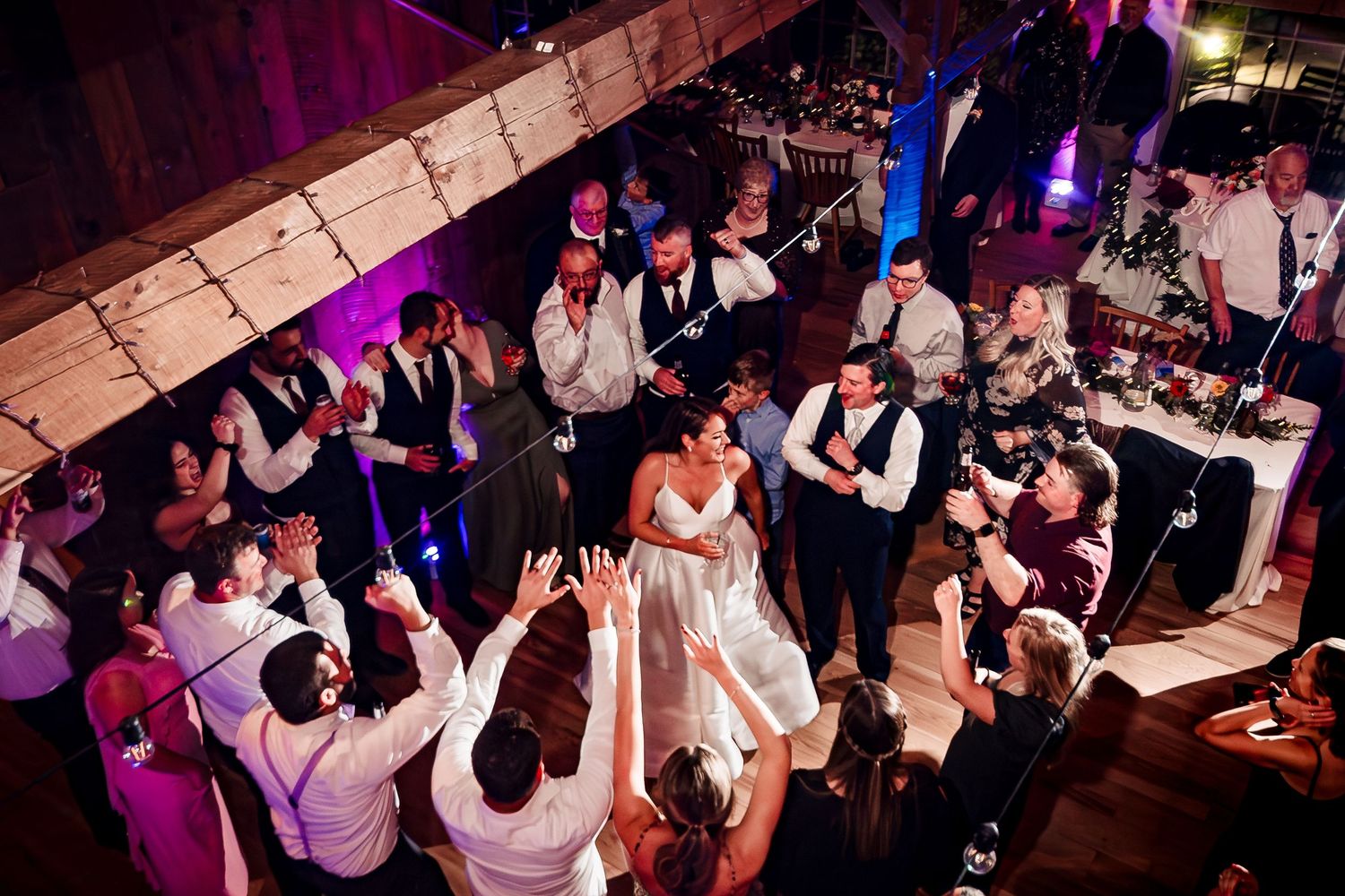 Wedding guests dance and celebrate on a dimly lit dance floor with purple lighting. Bittersweet Farm Rhode island wedding.