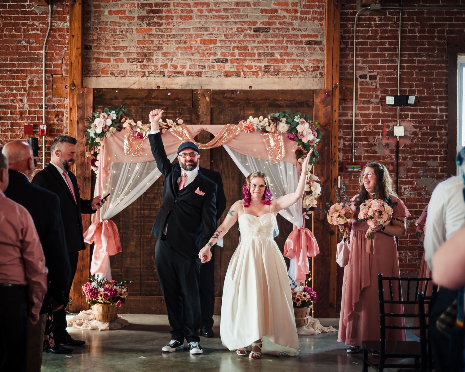 Wedding group poses against industrial brick wall backdrop at The Guild Brewery in Rhode island, Taken by Rhode Island wedding Photographer