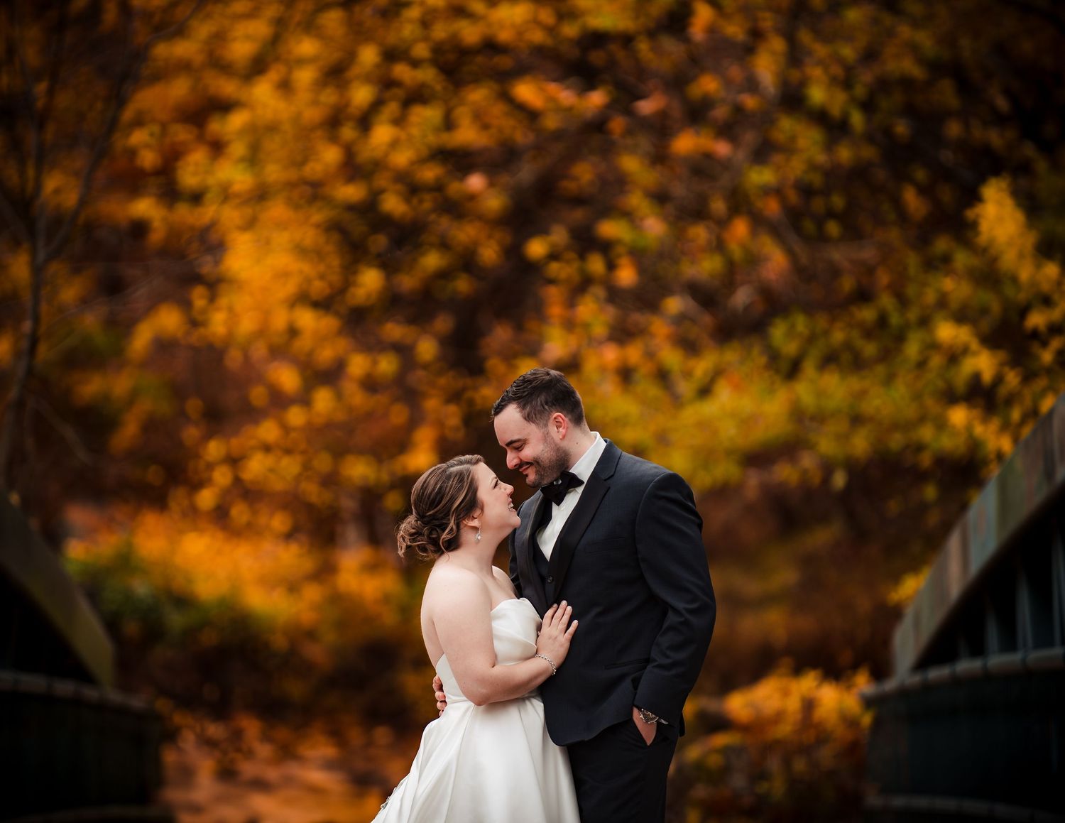 A romantic wedding couple poses in front of vibrant autumn foliage at sunset. Taken by Rhode Island wedding Photographer