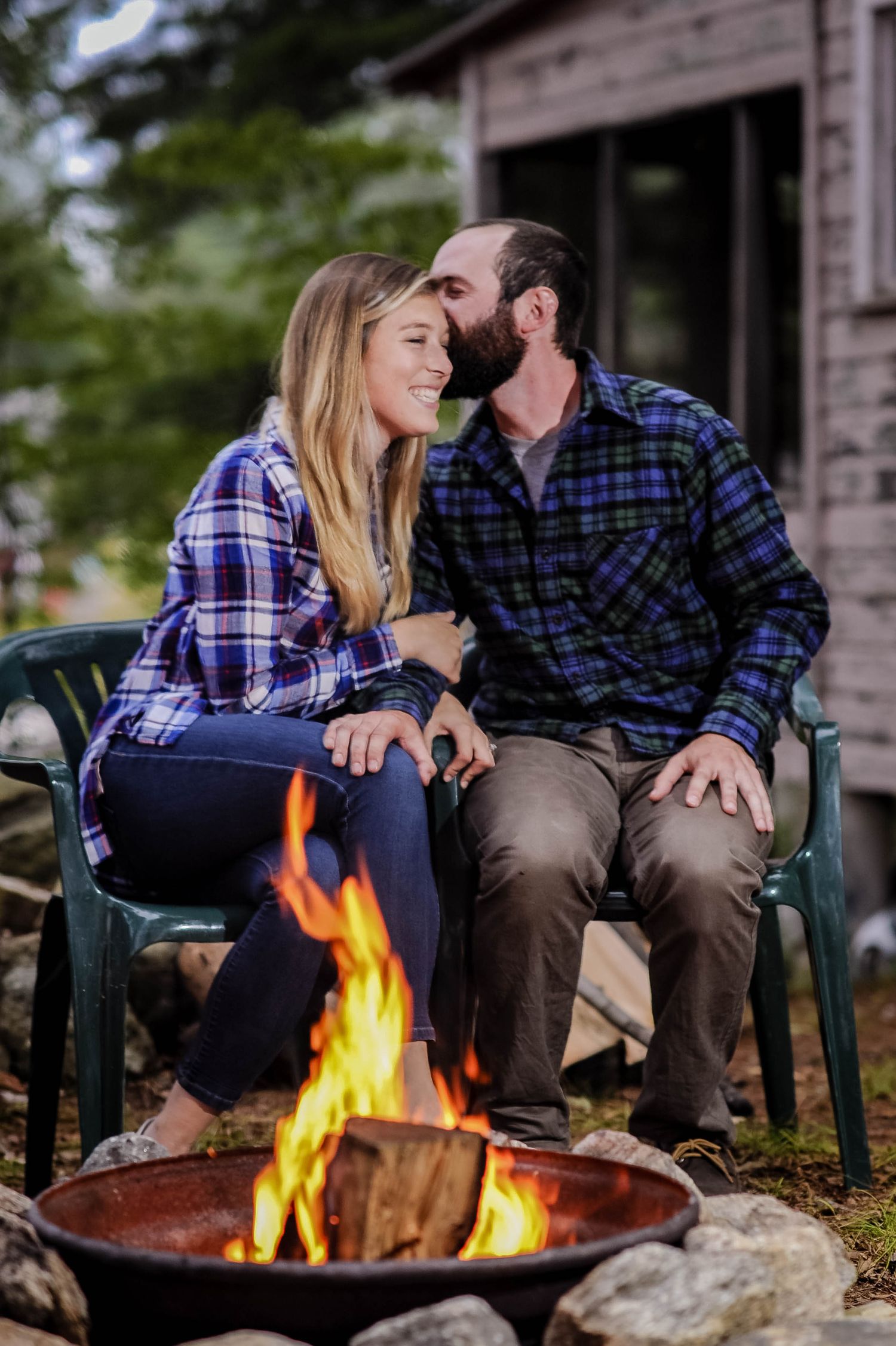 Cozy couple sits by an outdoor fire pit near a rustic Rhode Island cabin, photographed by a Rhode Island photographer.
